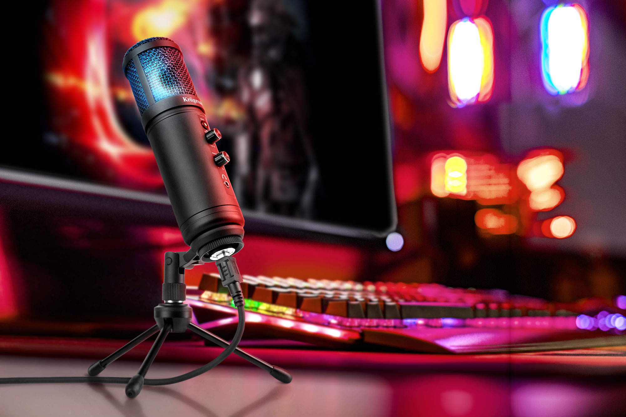 Czarny mikrofon z niebieską siateczką stoi na małym statywie. Klawiatura i monitor znajdują się w rozmytym tle.