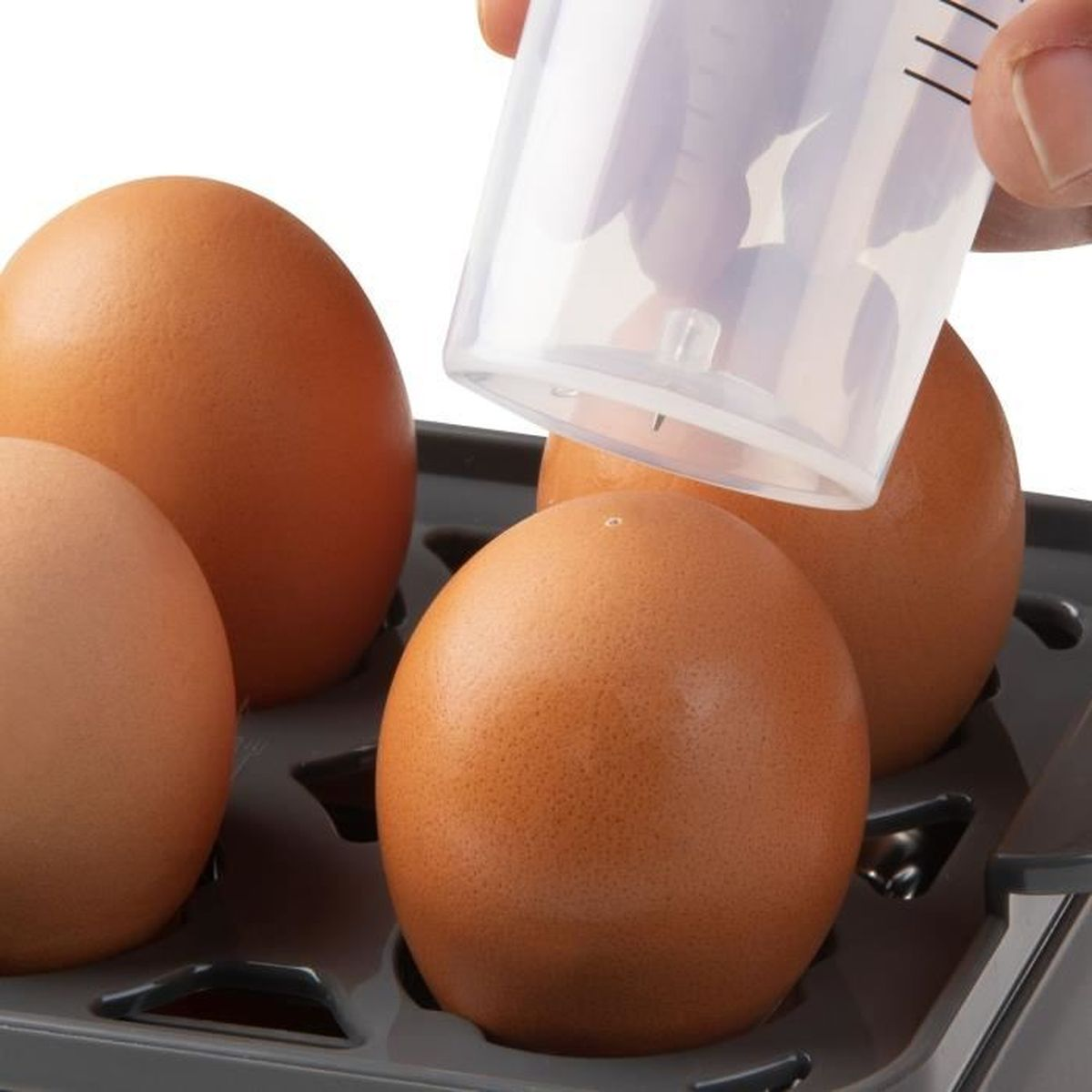 Brązowe jajka w tacy są napełniane wodą z przezroczystego kubka z miarką. Ręka trzyma kubek.