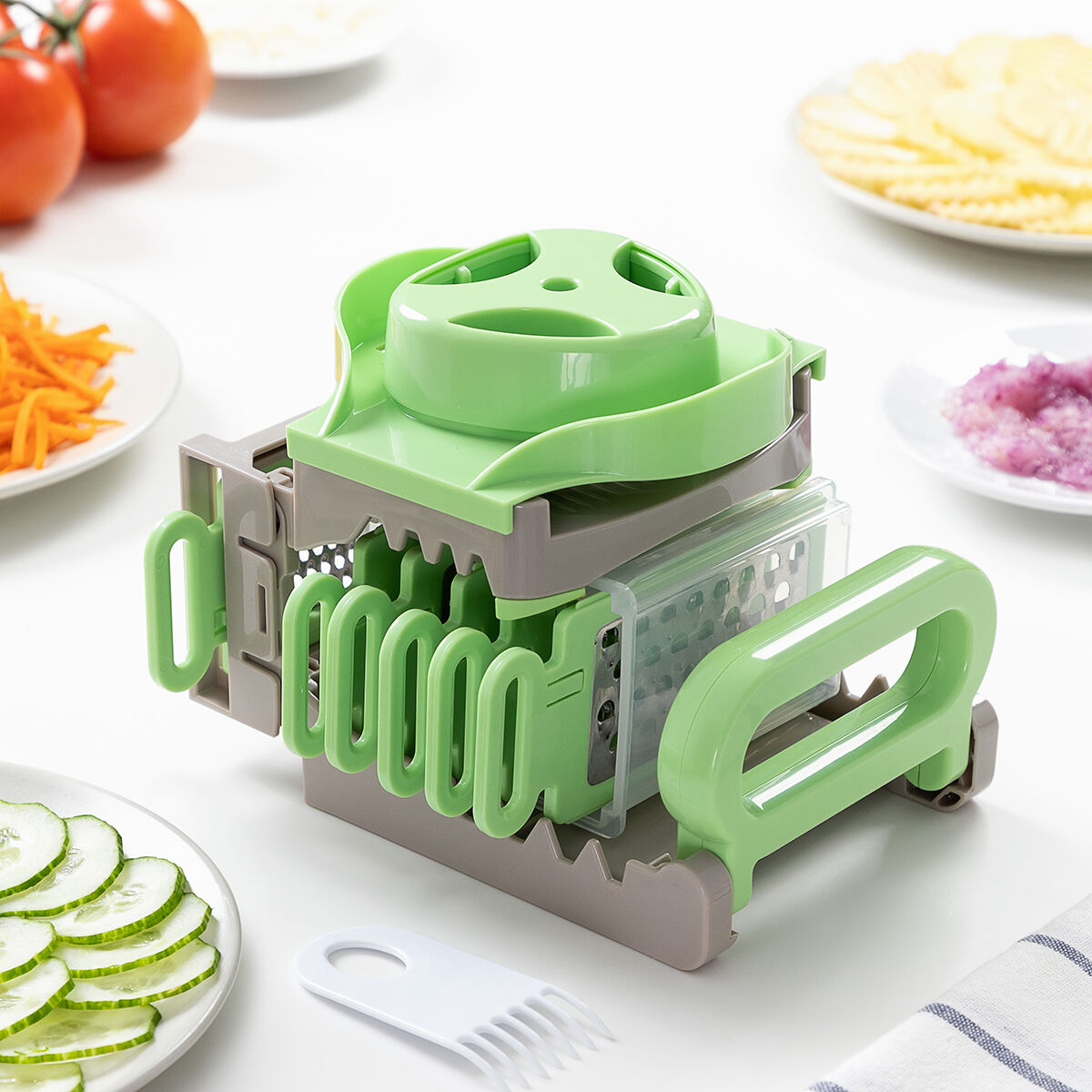 Un affettatrice di verdure verde e grigia con varie verdure preparate intorno, tra cui pomodori, carote e cetrioli a fette.