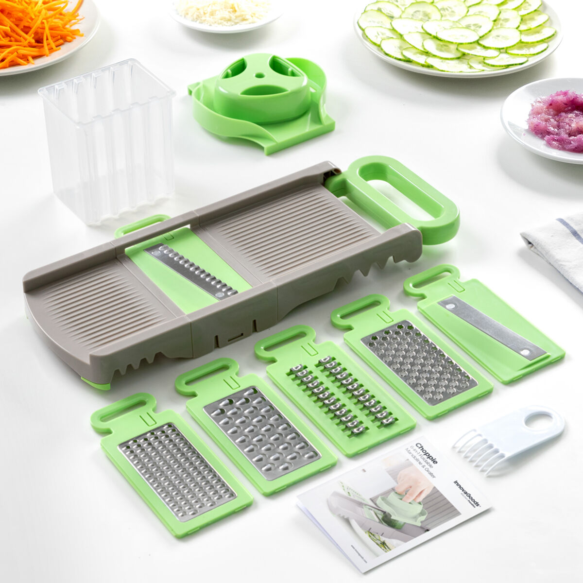 Un'affettatrice per verdure con più lame e accessori, insieme a carote, cetrioli e altri ingredienti affettati su una superficie bianca.