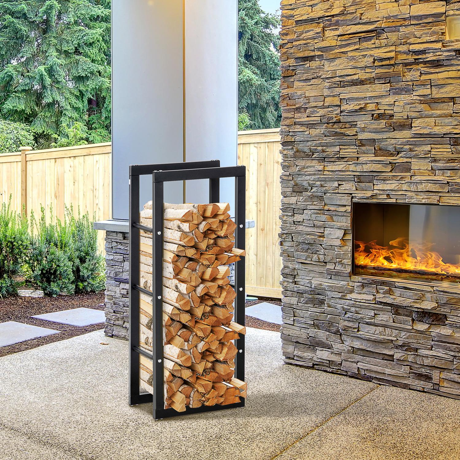 Ein schwarzer Metall-Brennholzständer mit gefüllten Holzscheiten steht auf einer Terrasse. Im Hintergrund ist ein Steinkamin mit Flammen zu sehen.