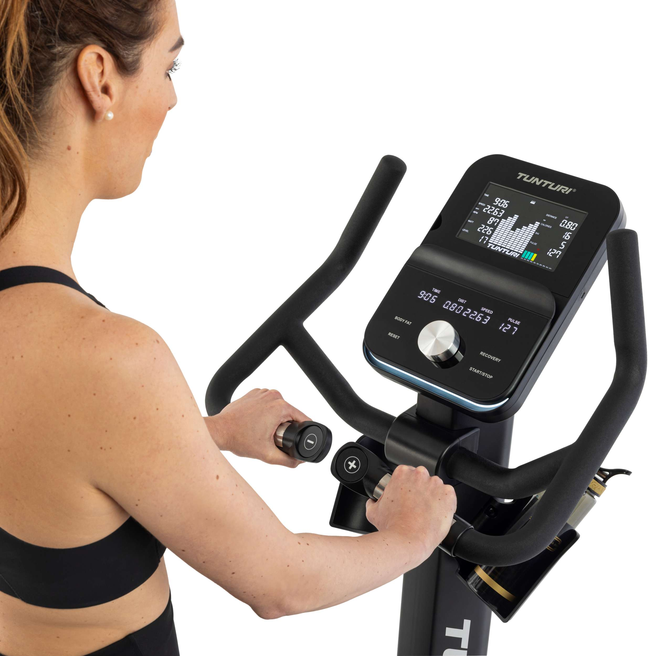 Vrouw op hometrainer. Display toont statistieken. Ze draagt een zwarte top.