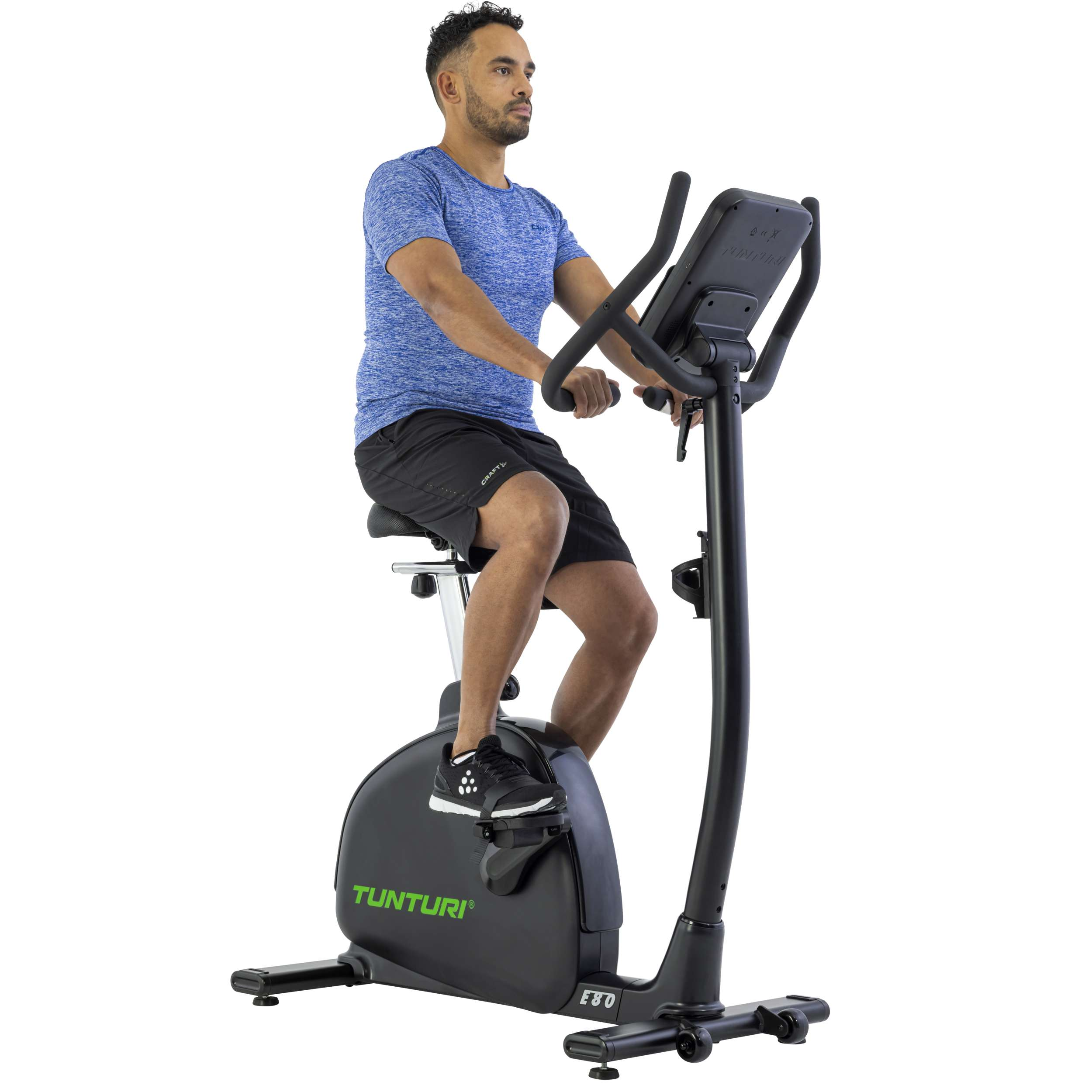 Man op hometrainer. Hij draagt een blauw shirt en een zwarte korte broek. De fiets is zwart met een digitaal display.