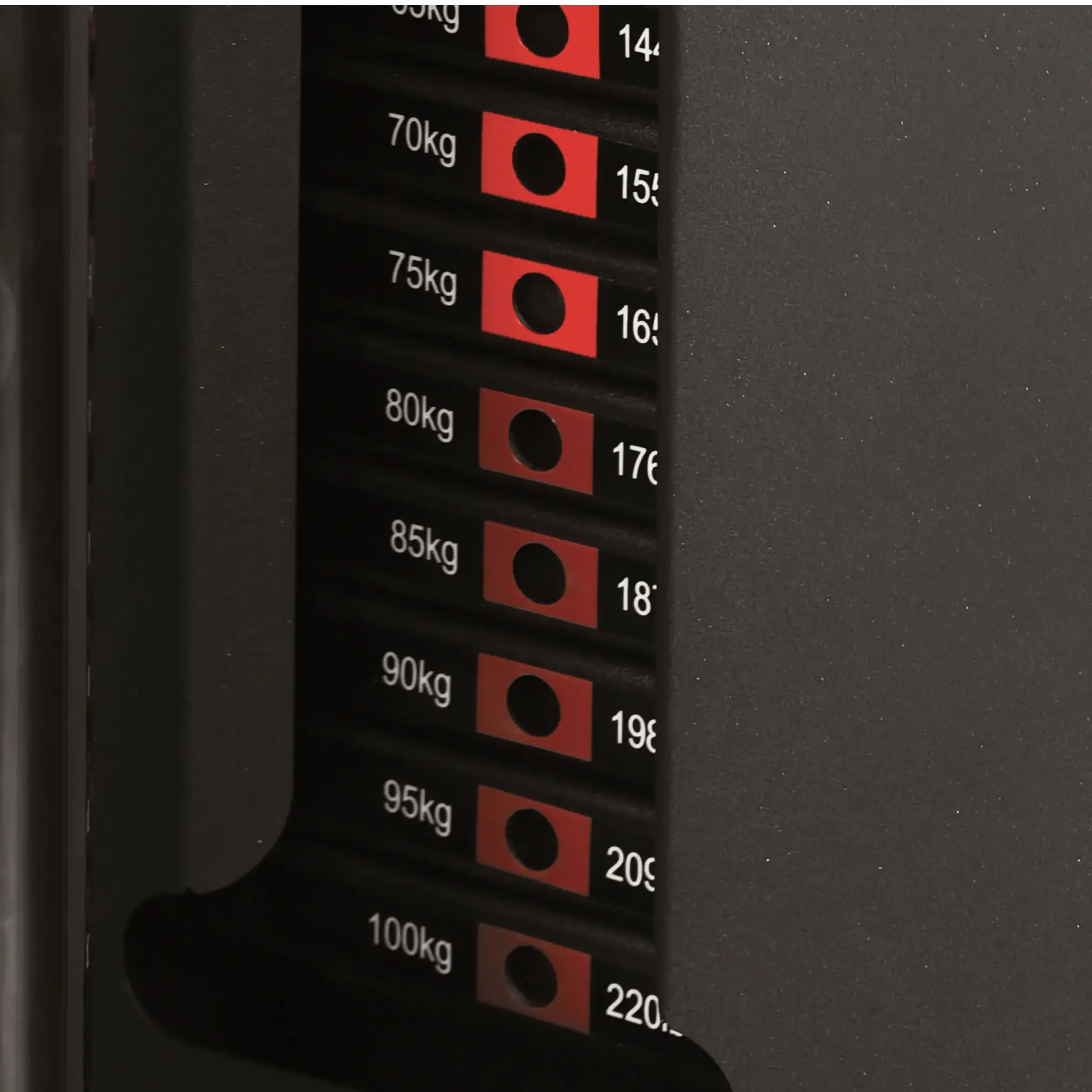 Close-up of a weight machine panel. It shows weight levels in kg and corresponding adjustment points, including red indicator lights.
