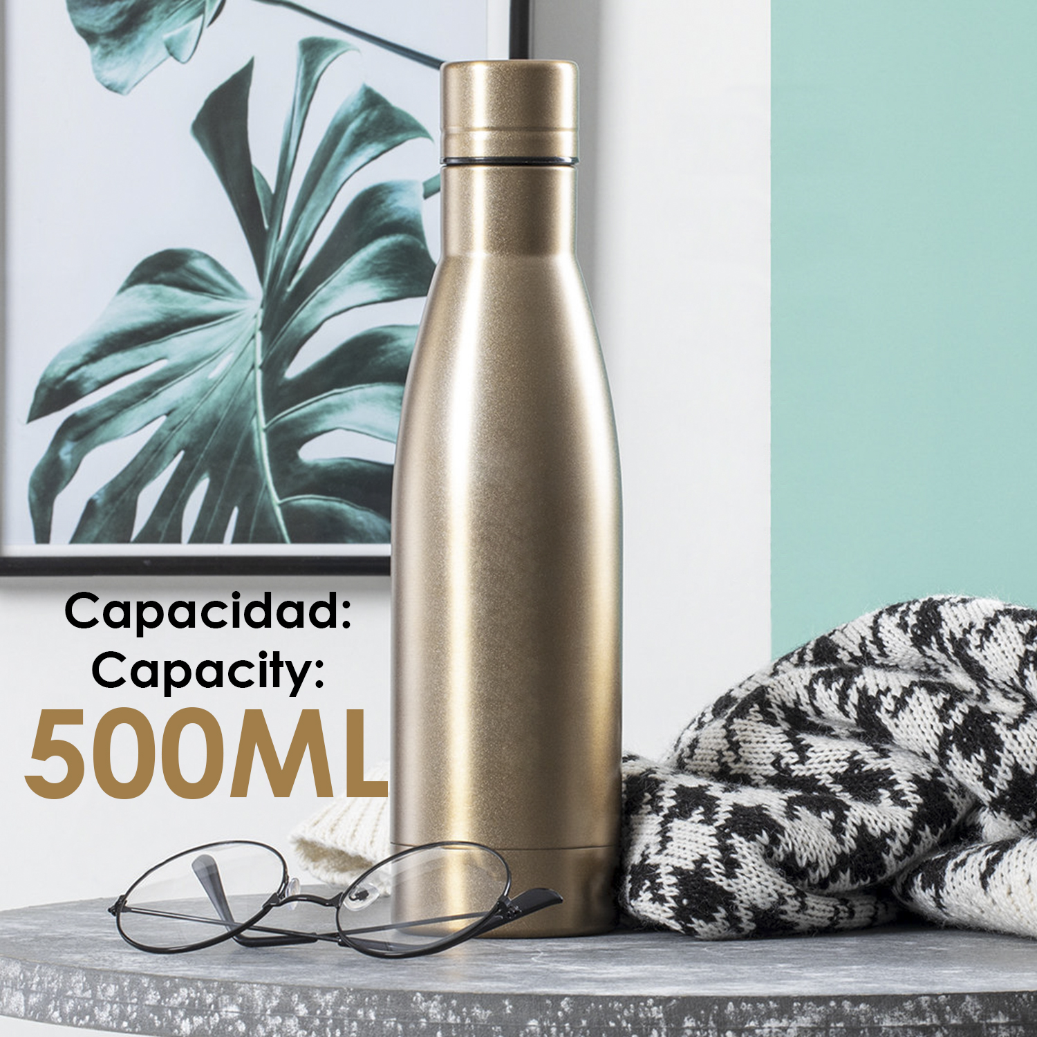 Una botella de agua dorada, gafas y un suéter están sobre una mesa. En el fondo hay un cuadro enmarcado de una planta.