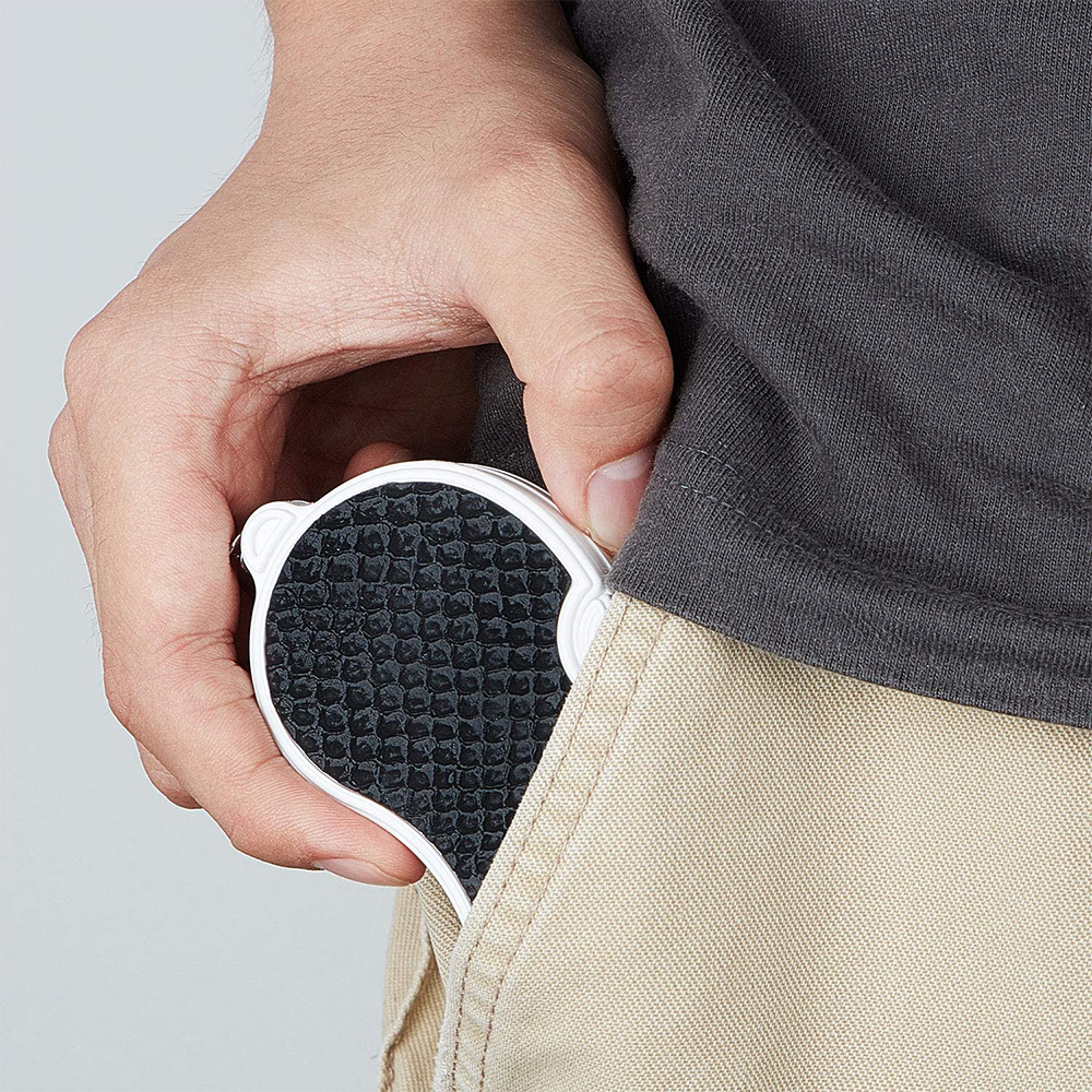 Eine Hand hält einen weiß-schwarzen, taschengroßen Gegenstand, der sich teilweise in einer Tasche befindet. Die Person trägt ein graues Hemd und eine beige Hose.