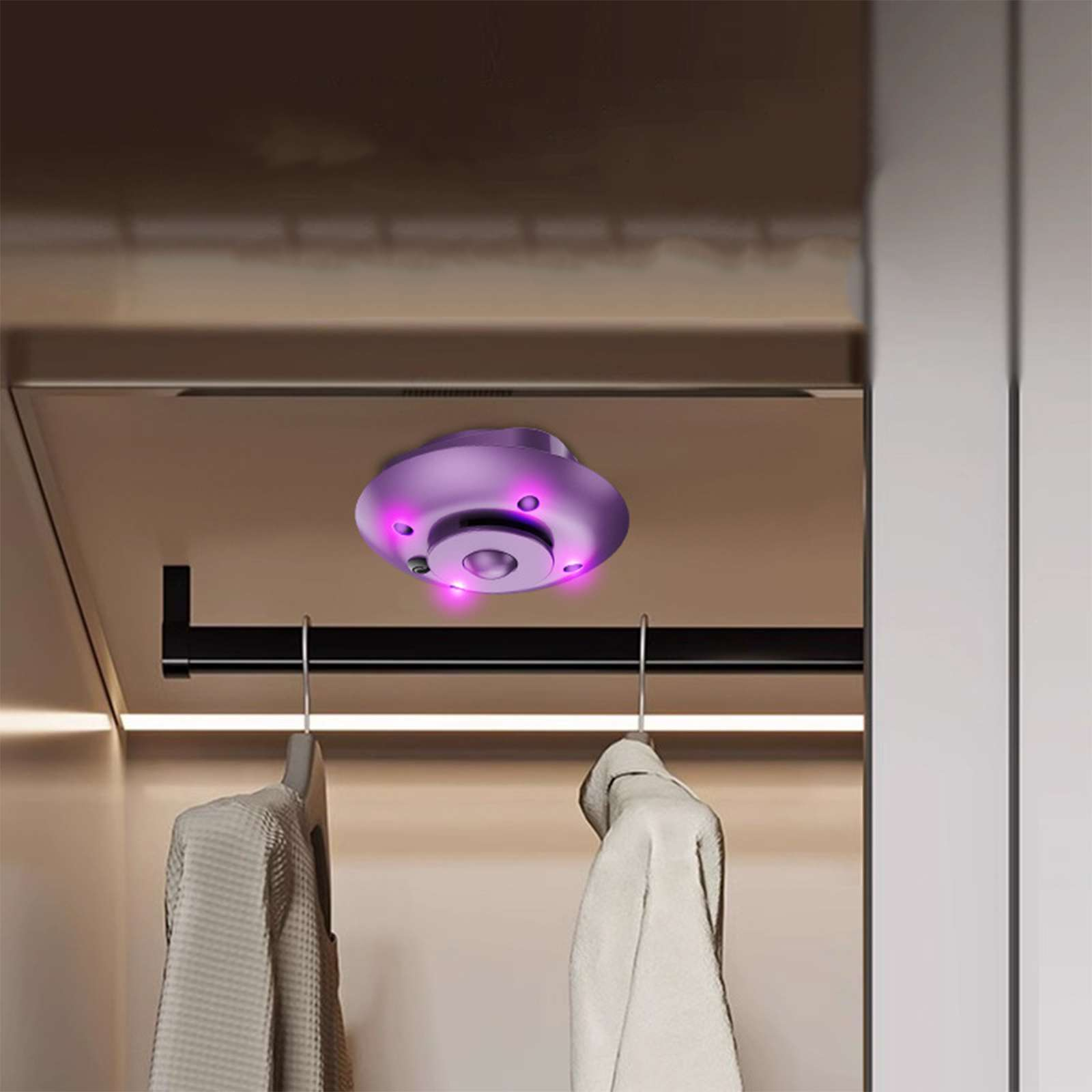 Ein lila Gerät mit Lichtern ist in einem Schrank montiert. Kleidung hängt darunter. Das Gerät befindet sich im oberen Teil des Bildes.