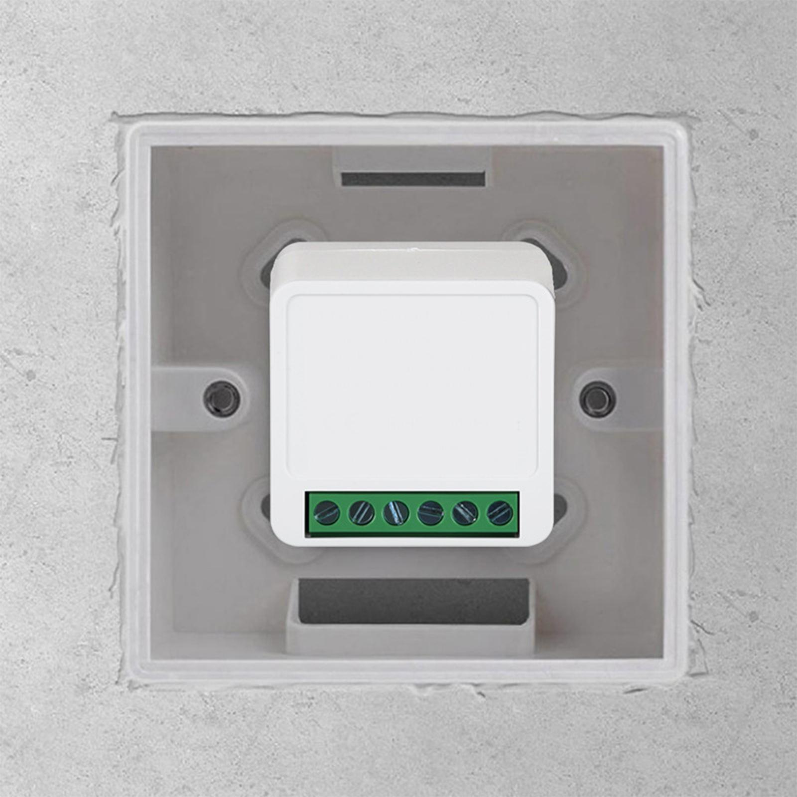 Ein weißes elektrisches Bauteil mit grünem Klemmenblock ist in einer grauen Unterputzdose in einer Betonwand installiert.