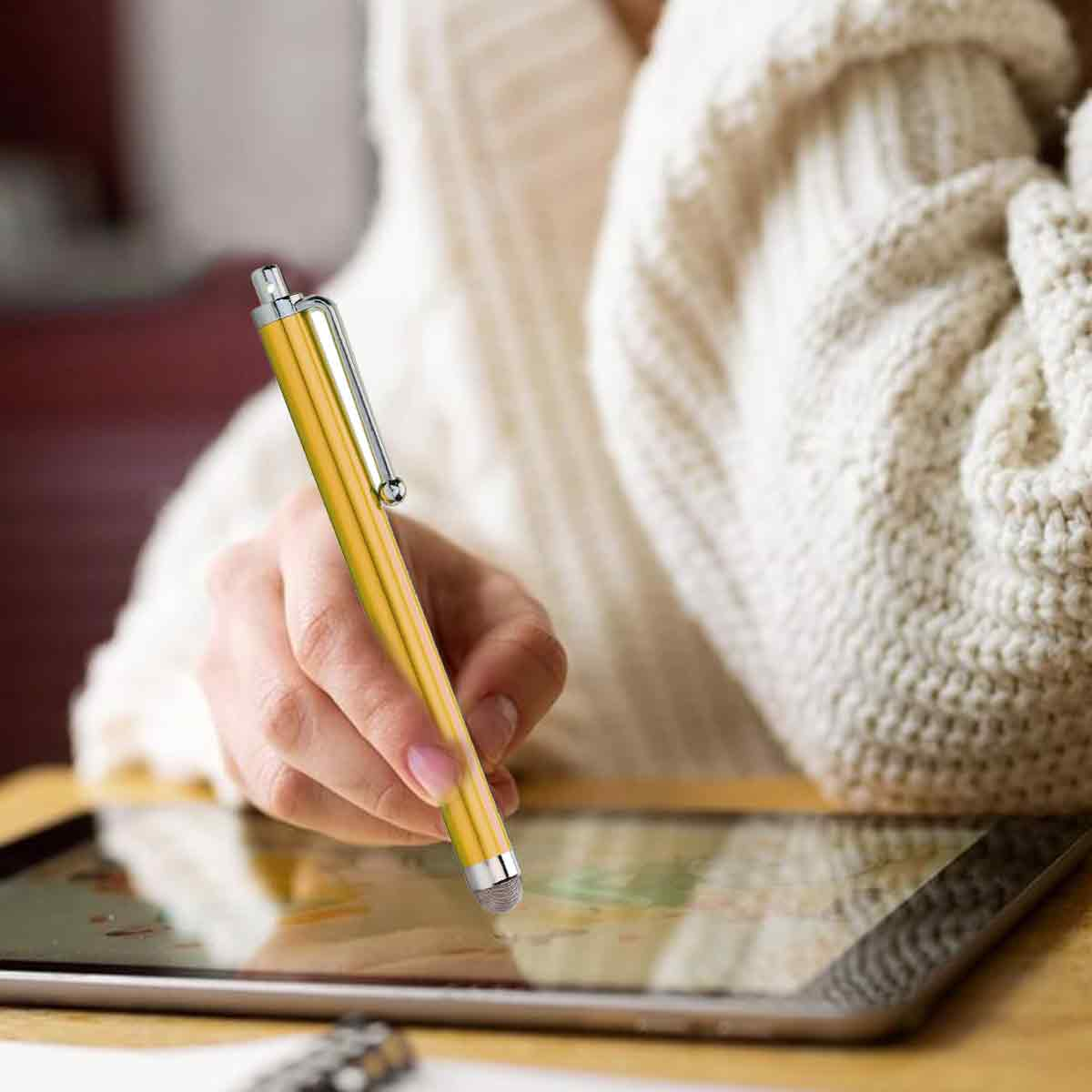 Eine Hand, die einen gelben Stift hält und ein Tablet berührt. Die Person trägt einen weißen Pullover. Der Stift hat einen silbernen Clip.