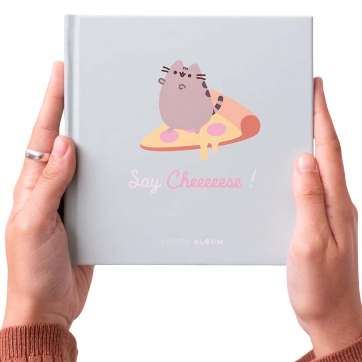Mains tenant un album photo. La couverture montre un chat sur une pizza avec le texte 'Say Cheeeese!' et 'PHOTO ALBUM'.