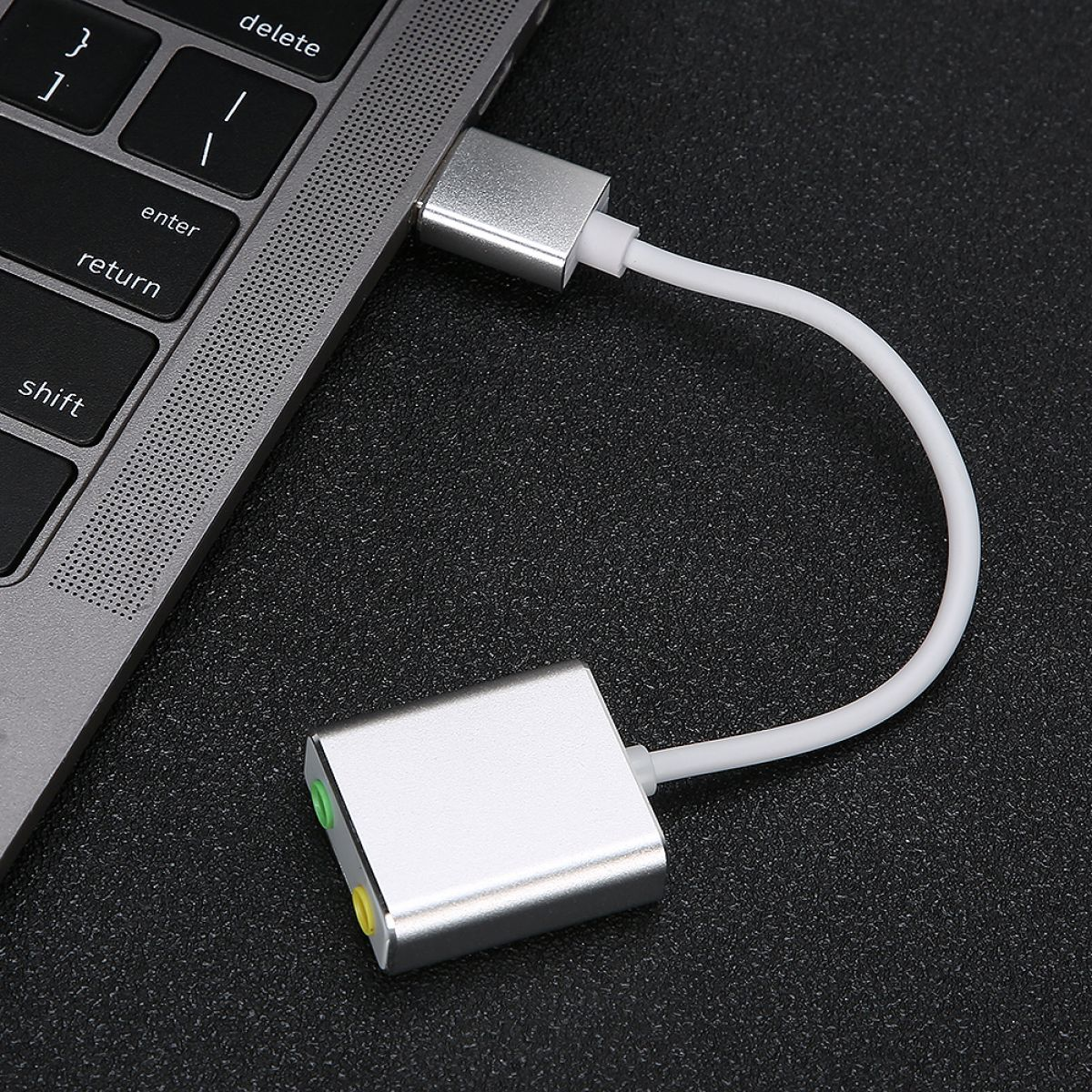 Ein silberner Adapter verbindet sich mit einem Laptop, mit einem weißen Kabel, das zu einem anderen silbernen Adapter mit grünen und gelben Buchsen führt.