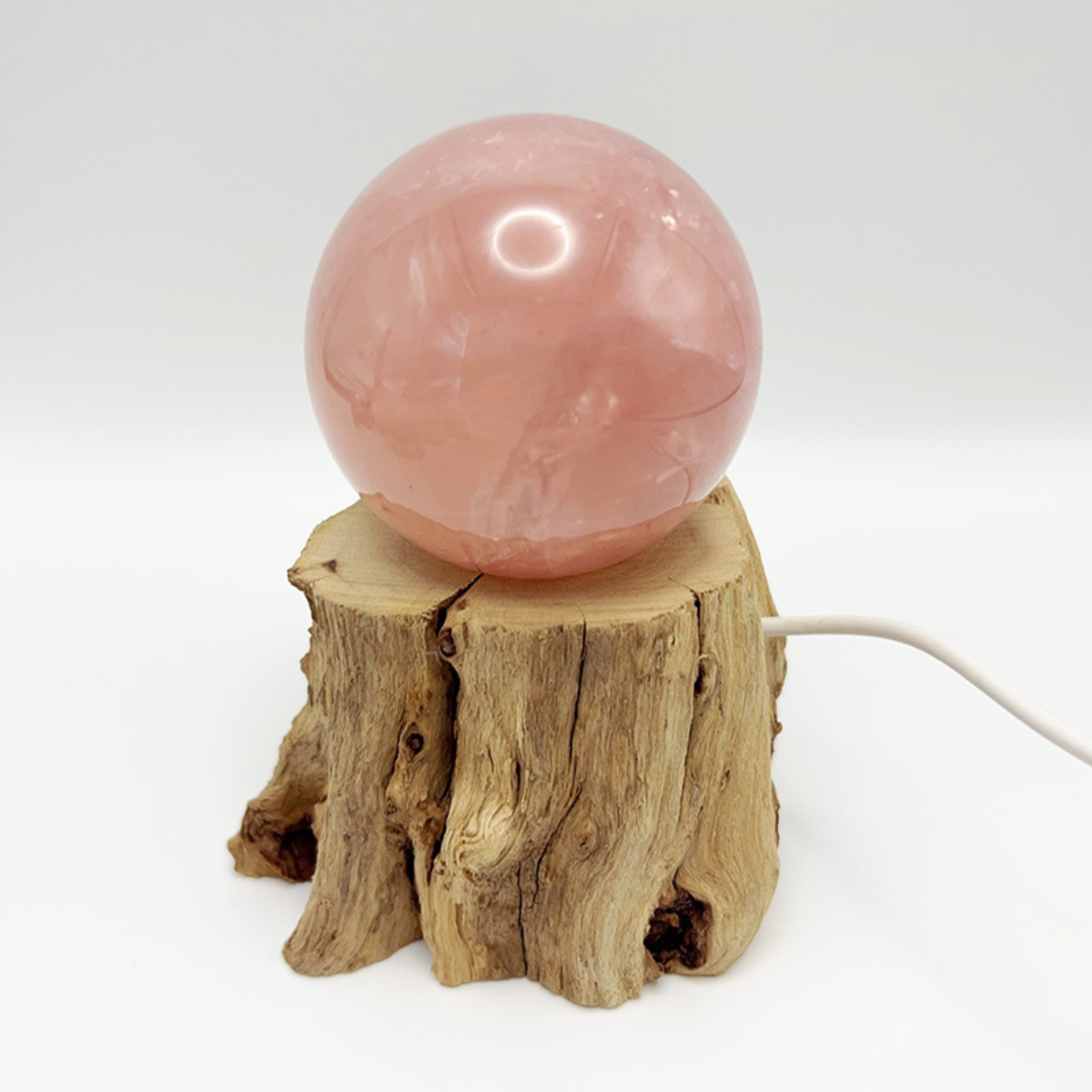 Ein rosa Kristallkugel steht auf einem Holzständer. Ein weißes Kabel geht vom Ständer aus. Der Hintergrund ist schlicht weiß.