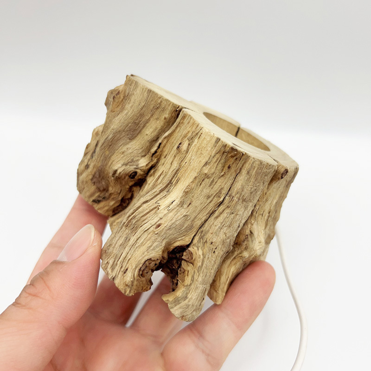 Eine Hand hält einen kleinen, verwitterten Holzblock mit zwei Löchern. Das Holz ist hellbraun mit sichtbarer Maserung auf weißem Hintergrund.