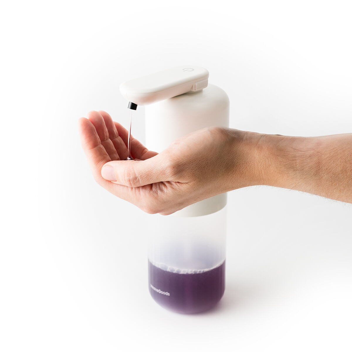 Una mano è sotto un dispenser di sapone bianco. Il sapone liquido viene erogato sulla mano. Il sapone è viola e lo sfondo è bianco.