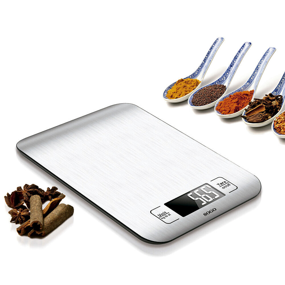 Una bilancia da cucina digitale argentata con display che mostra 56,5. Cucchiai pieni di spezie e anice stellato e bastoncini di cannella sono accanto.