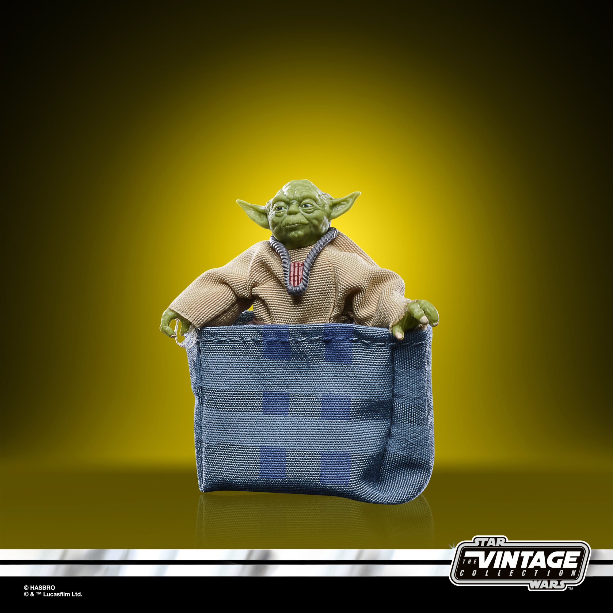 Mavi bir çantada Yoda oyuncağı. Yeşil ten, bej elbise ve mavi bir çanta. Sarı arka plan.