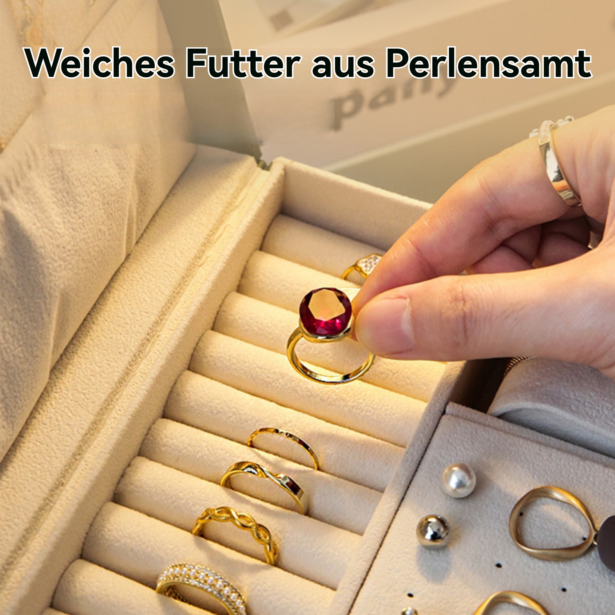 Eine Hand hält einen goldenen Ring mit einem roten Edelstein in einer Schmuckschatulle. Andere Ringe befinden sich in der Schachtel.