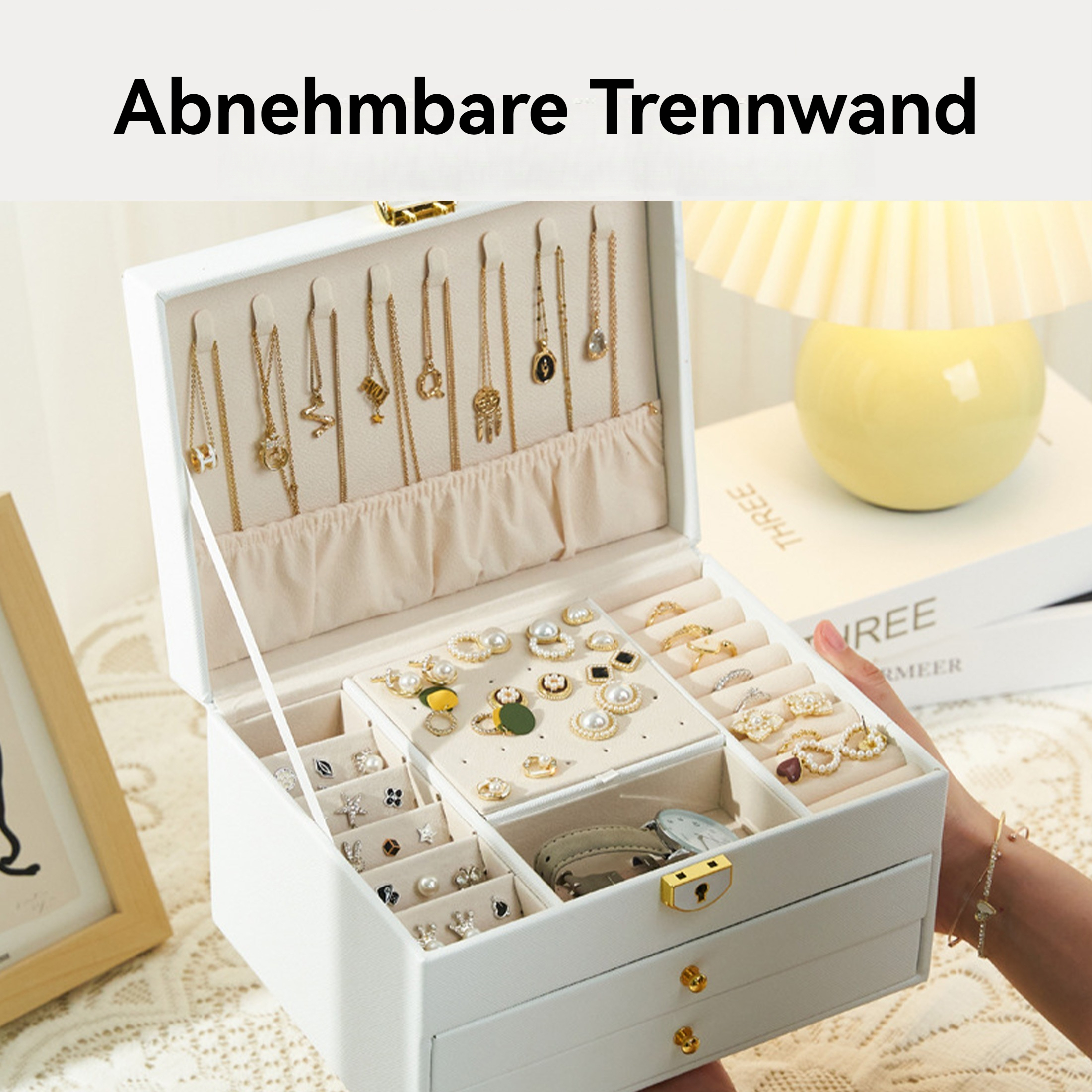 Offene weiße Schmuckschatulle mit verschiedenen goldenen Halsketten, Ringen und Ohrringen. Eine Hand hält die Box. Im Hintergrund eine gelbe Lampe.