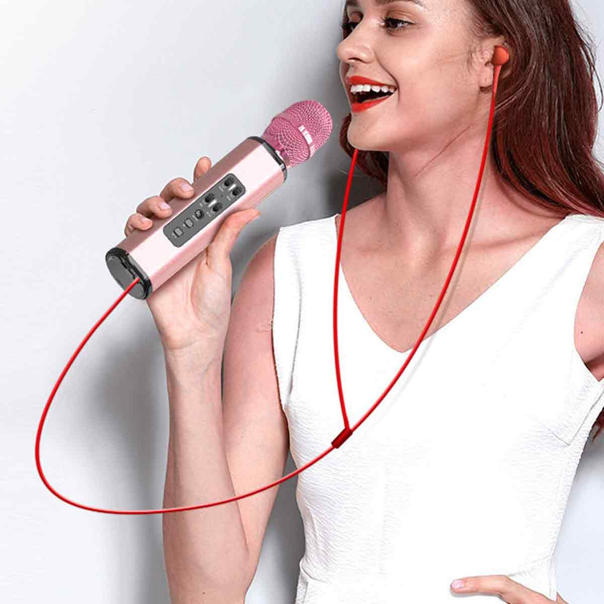 Eine Frau hält ein pinkfarbenes Mikrofon und trägt rote Ohrhörer. Sie trägt ein weißes Oberteil und lächelt. Der Hintergrund ist schlicht.
