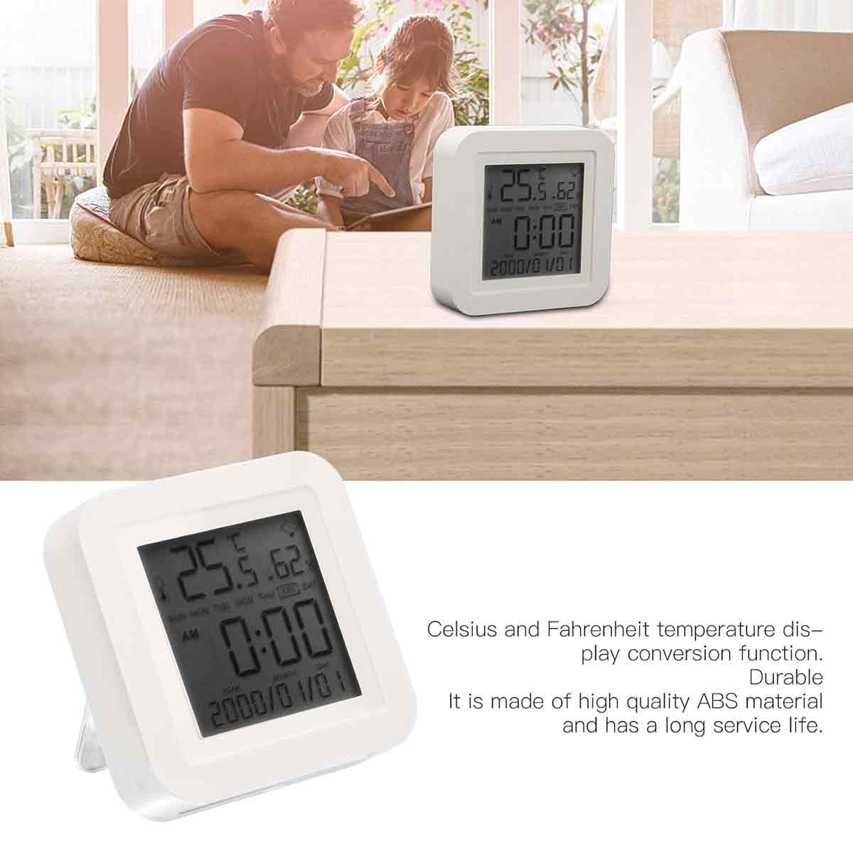Eine Digitaluhr zeigt 25,5 Grad an. Im Hintergrund sind ein Mann und ein Kind. Die Uhr steht auf einem Holztisch.