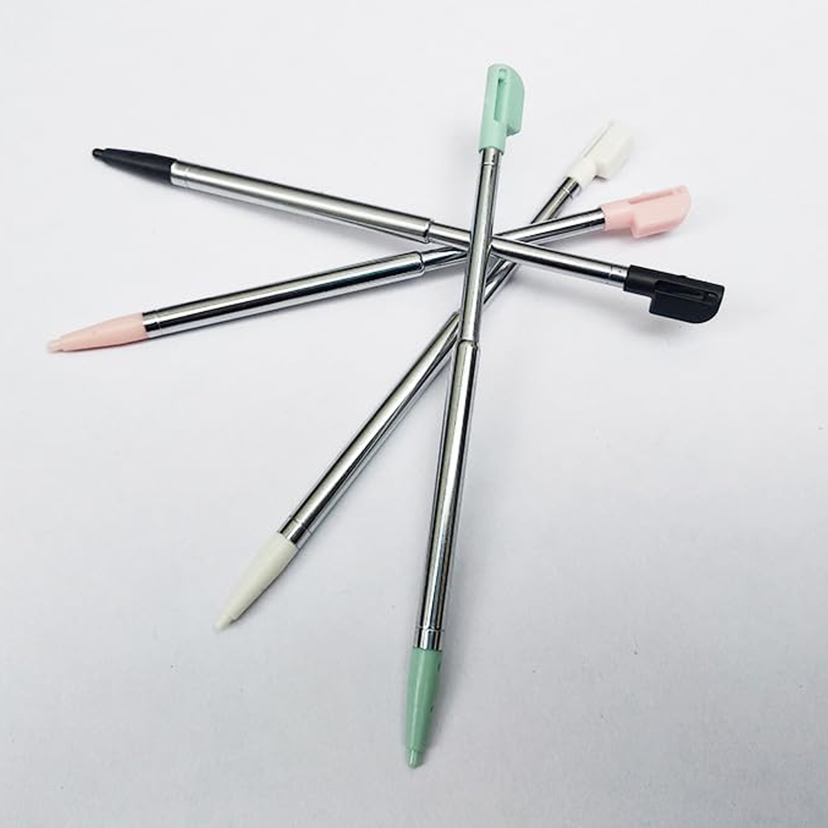 Mehrere Stifte mit silbernen Schäften und unterschiedlich farbigen Spitzen (schwarz, rosa, weiß und grün) sind auf einer weißen Oberfläche angeordnet.