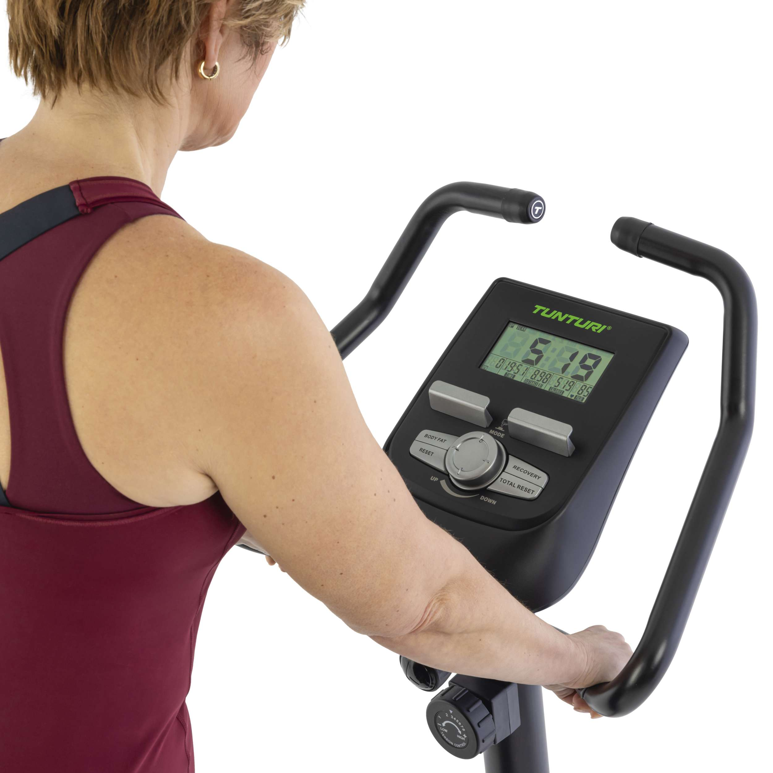 Vrouw die een Tunturi hometrainer gebruikt. Het display toont statistieken. Ze draagt een bordeauxrode tanktop.