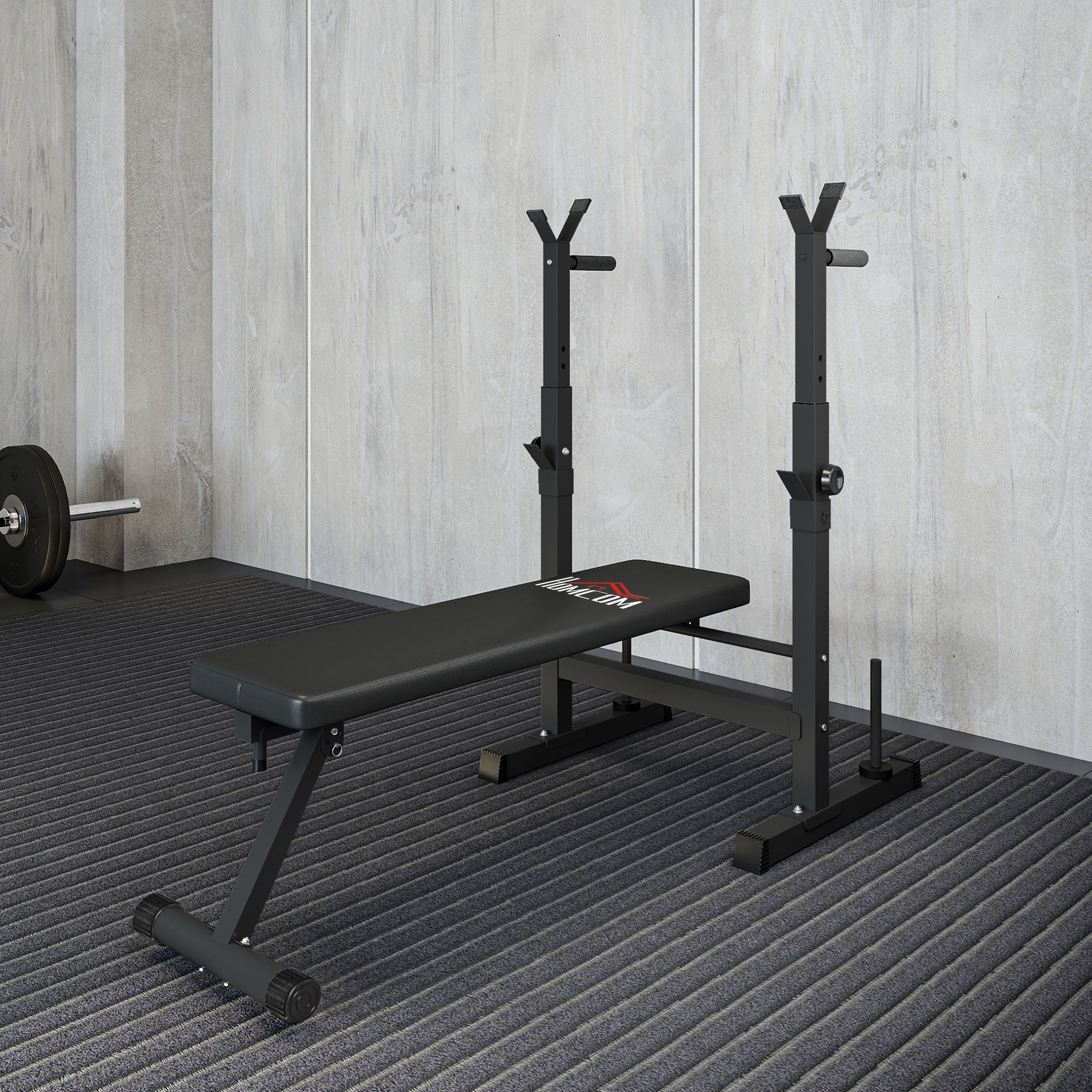 Una panca e un rack per pesi in palestra. Un bilanciere è appoggiato sul pavimento. Muri e pavimento grigi.