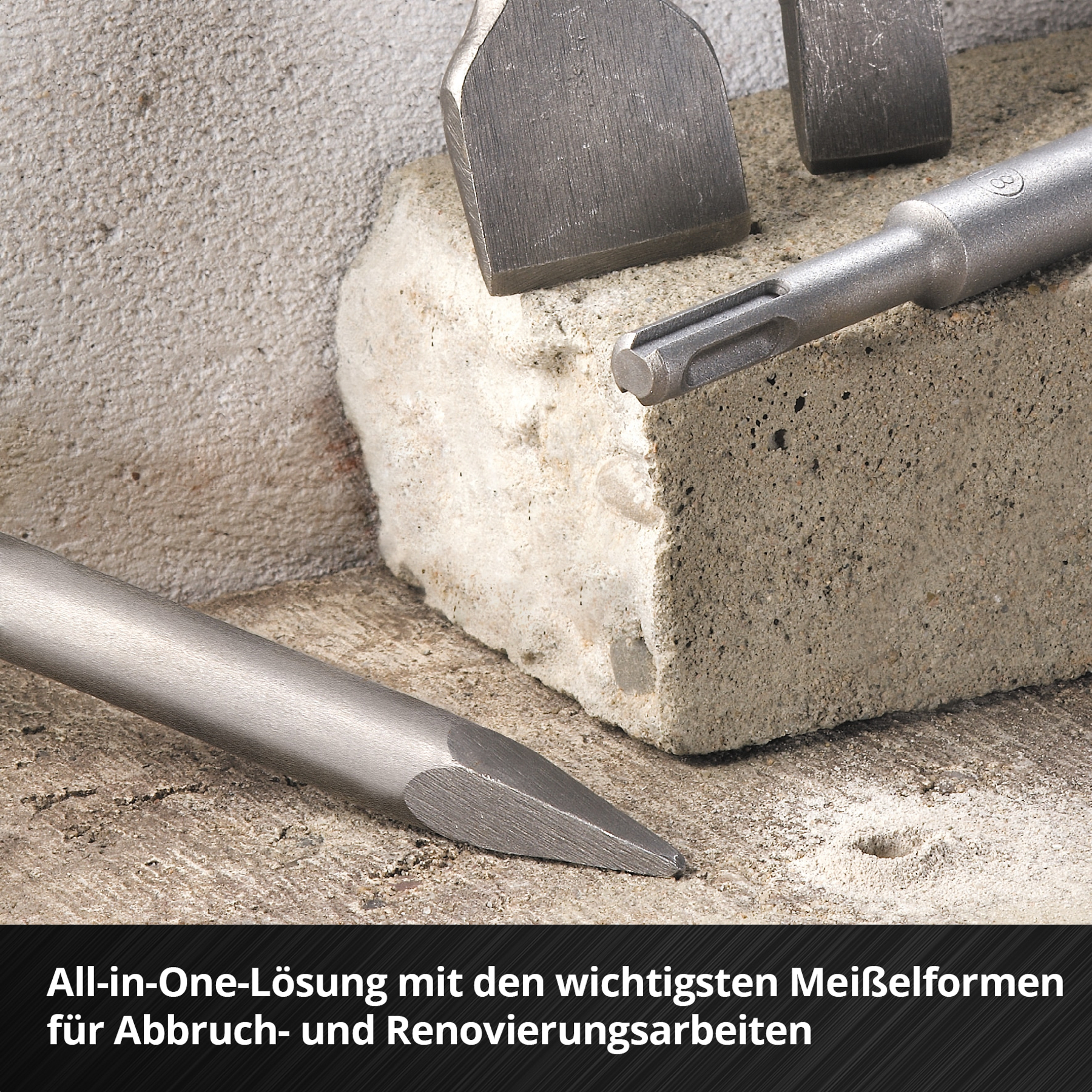 Nahaufnahme von Werkzeugen auf einer Steinoberfläche. Meißel und ein Bohrer sind zu sehen, mit einem hellgrauen Betonblock im Hintergrund.
