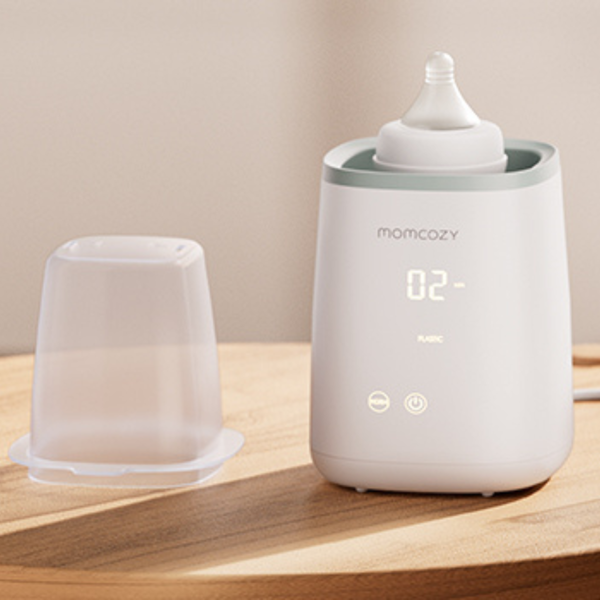 A white baby bottle warmer with a bottle inside and a clear plastic cup next to it on a wooden surface.