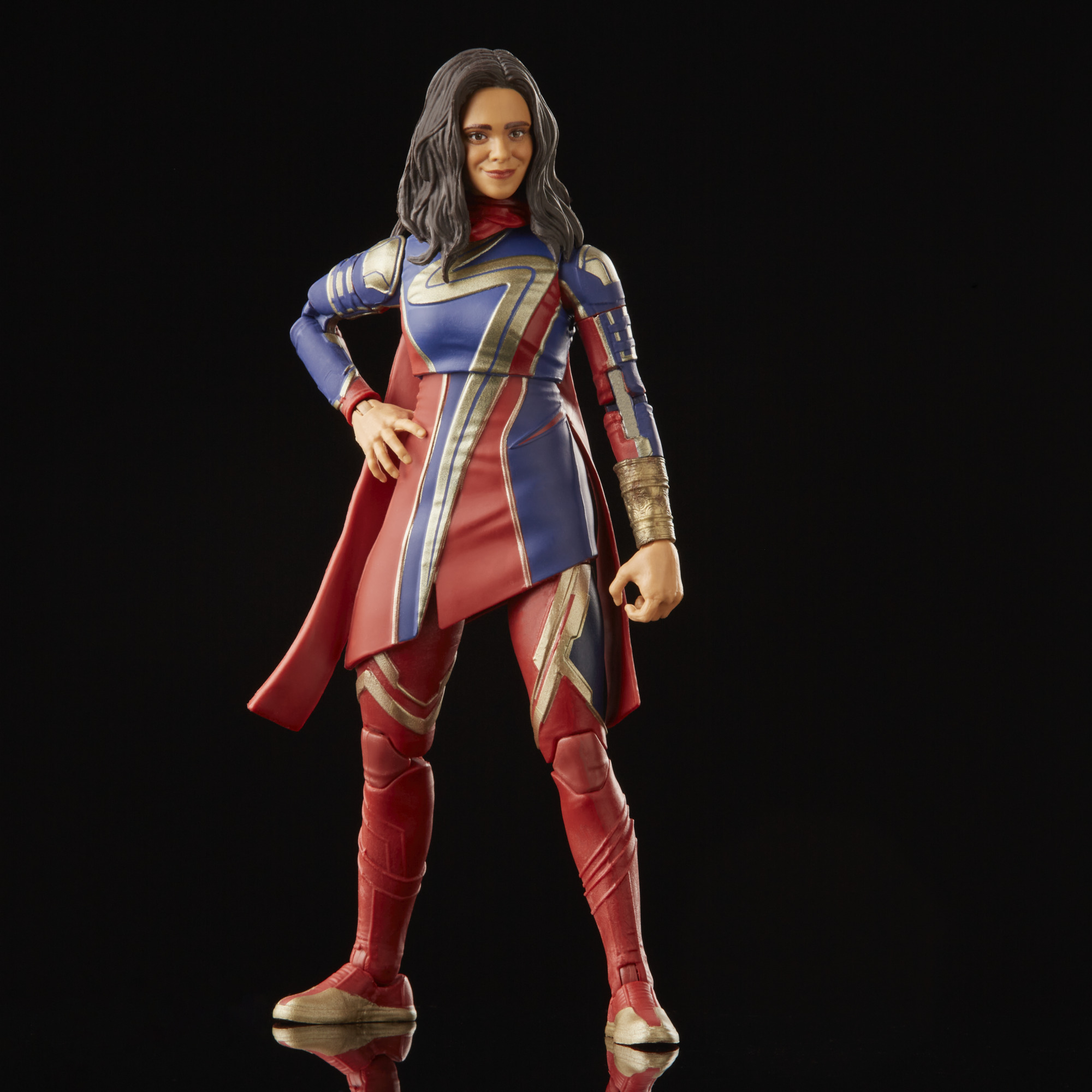 Figura de acción de una mujer con un disfraz de superhéroe rojo, azul y dorado, de pie con la mano en la cadera, sobre un fondo negro.