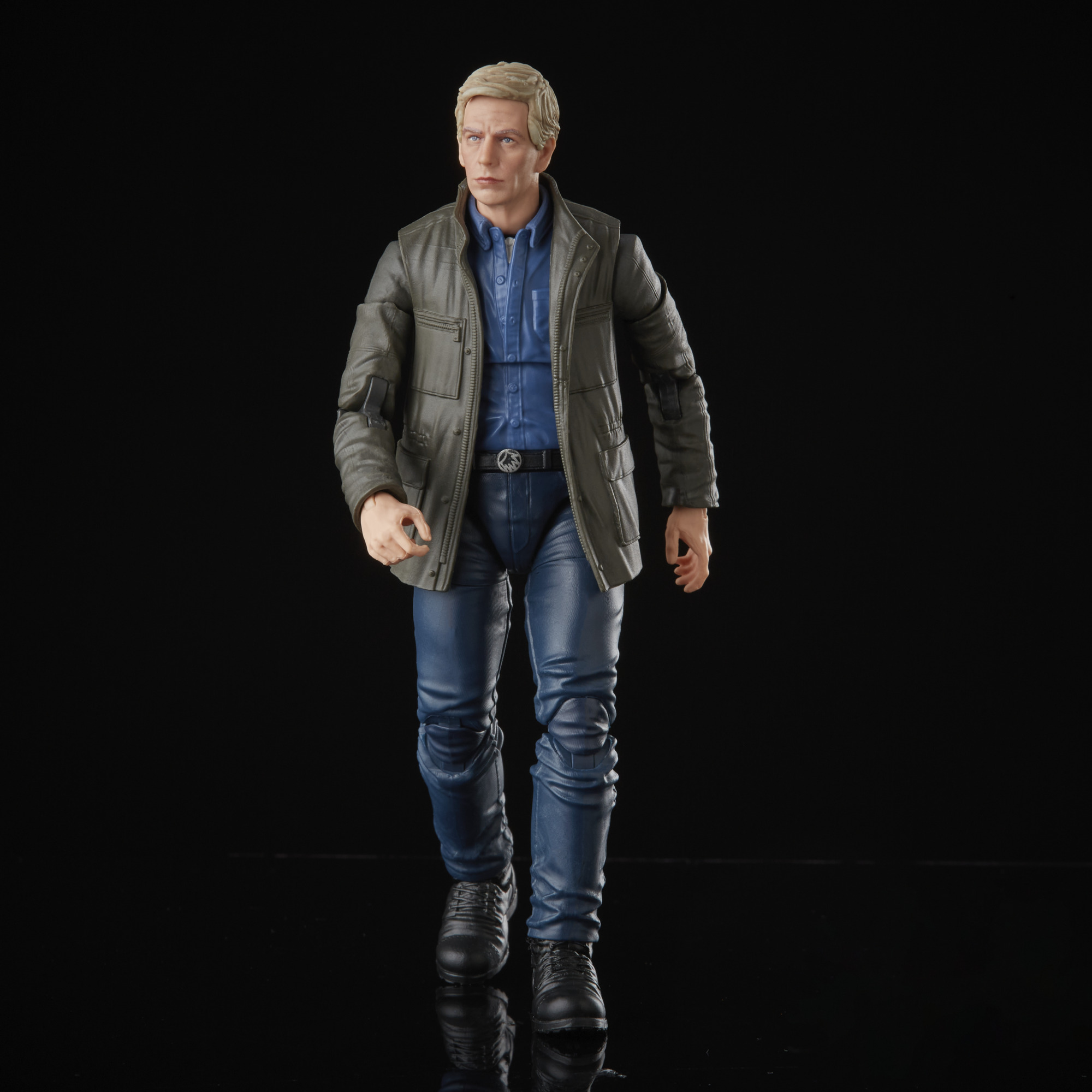 Una figura de un hombre con chaqueta gris, camisa azul y vaqueros. Camina hacia el espectador sobre un fondo negro.