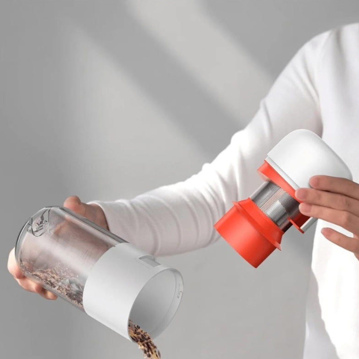A person holding a vacuum cleaner component. The container is clear with debris, while the other component is white and orange.