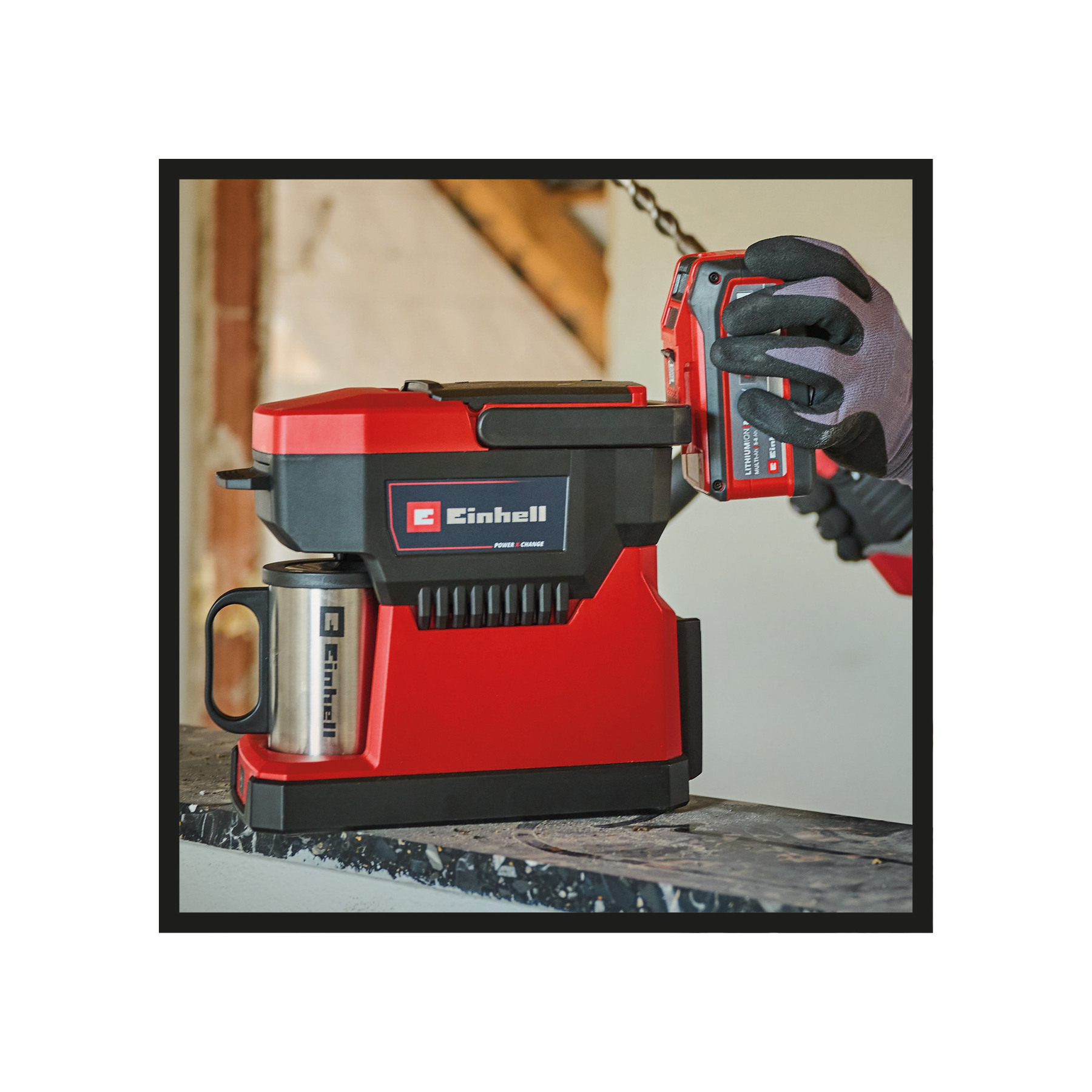 Czerwono-czarny ekspres do kawy Einhell ze stalowym kubkiem. Ręka w rękawicy trzyma baterię.