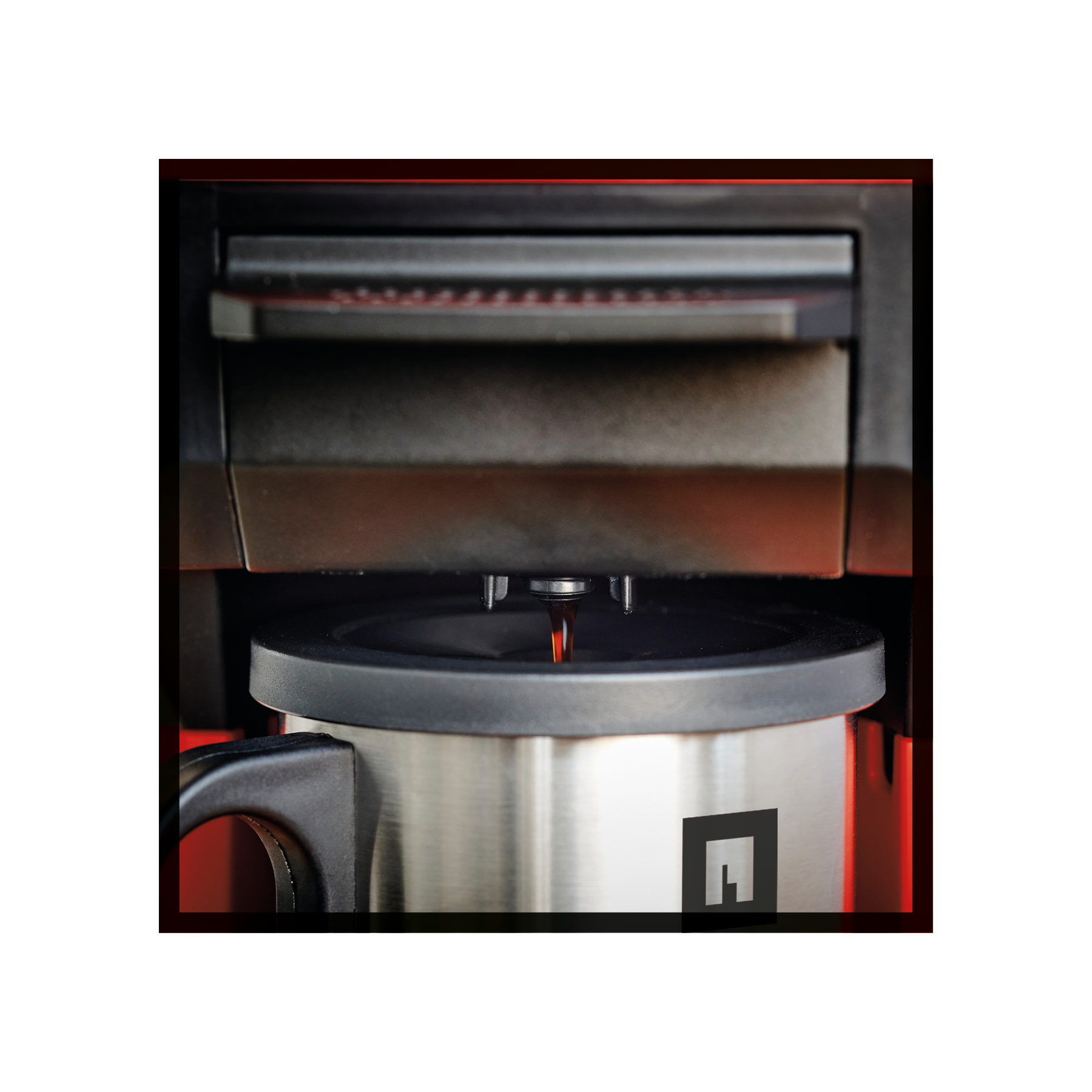 Ekspres do kawy dozuje kawę do kubka ze stali nierdzewnej. Widoczne czarne detale, czerwone akcenty i logo.