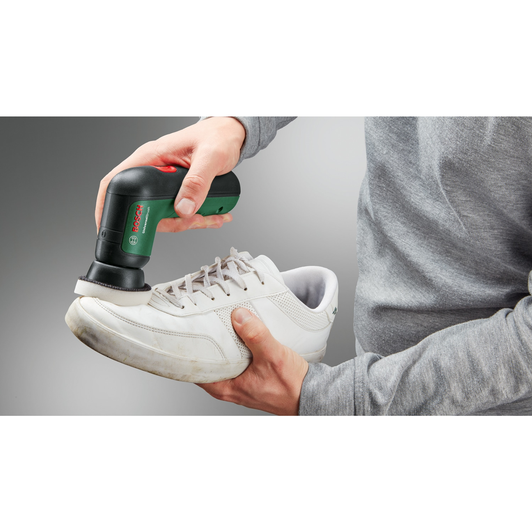 Eine Person reinigt mit einer Bosch UniversalBrush einen schmutzigen weißen Sneaker. Die Bürste ist grün und schwarz.