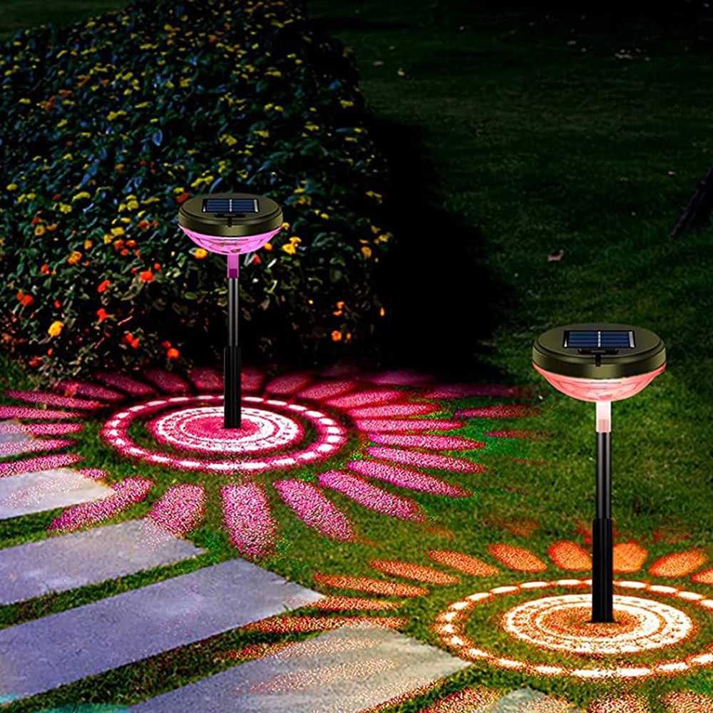 Zwei Solar-Gartenleuchten beleuchten einen Garten. Die Lichter werfen Muster auf das Gras. Im Hintergrund ein Busch mit Blumen.