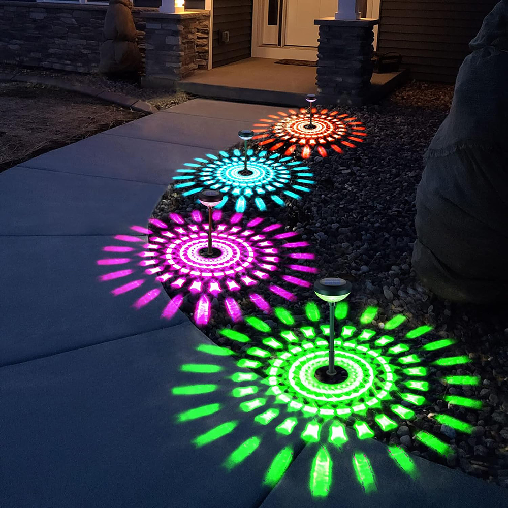 Weg beleuchtet von Solarleuchten mit farbigen Mustern: rot, blau, lila und grün. Lichter befinden sich auf einem Gehweg in der Nähe eines Hauses.