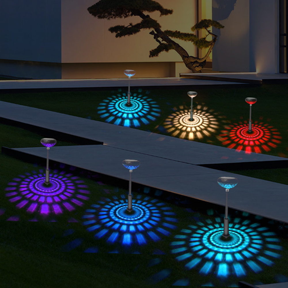 Gartenszene bei Nacht mit bunten Lichtern auf dem Rasen. Solarbetriebene Lampen werfen Muster in Blau, Rot und Lila.