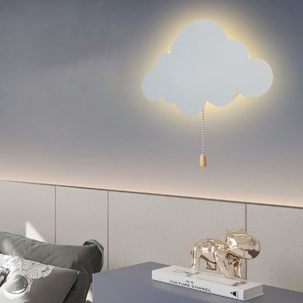 Wolkenförmige Wandlampe. Eine Kette hängt herunter. Tisch mit Deko und Kissen darunter. Graue Wand.