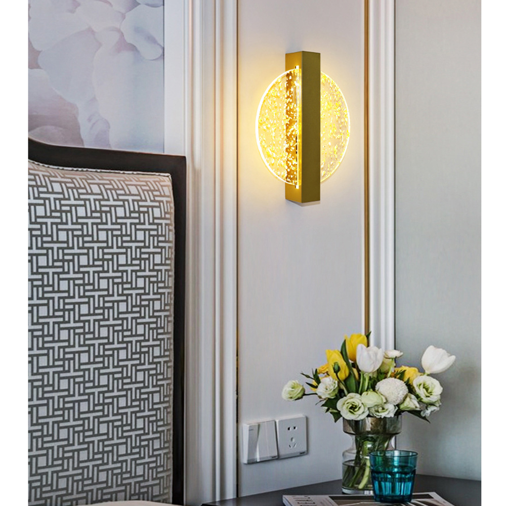 Wandlampe mit goldenem Rahmen und rundem, strukturiertem Glasschirm, über einem Tisch mit Blumen und einem Wasserglas.