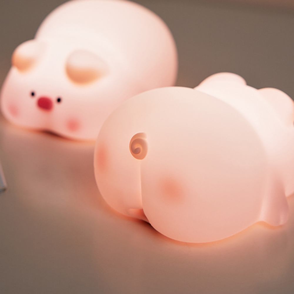 Zwei rosa schweineförmige Nachtlichter. Eines zeigt das Gesicht, das andere den Hintern. Beide haben rosige Wangen und sind beleuchtet.
