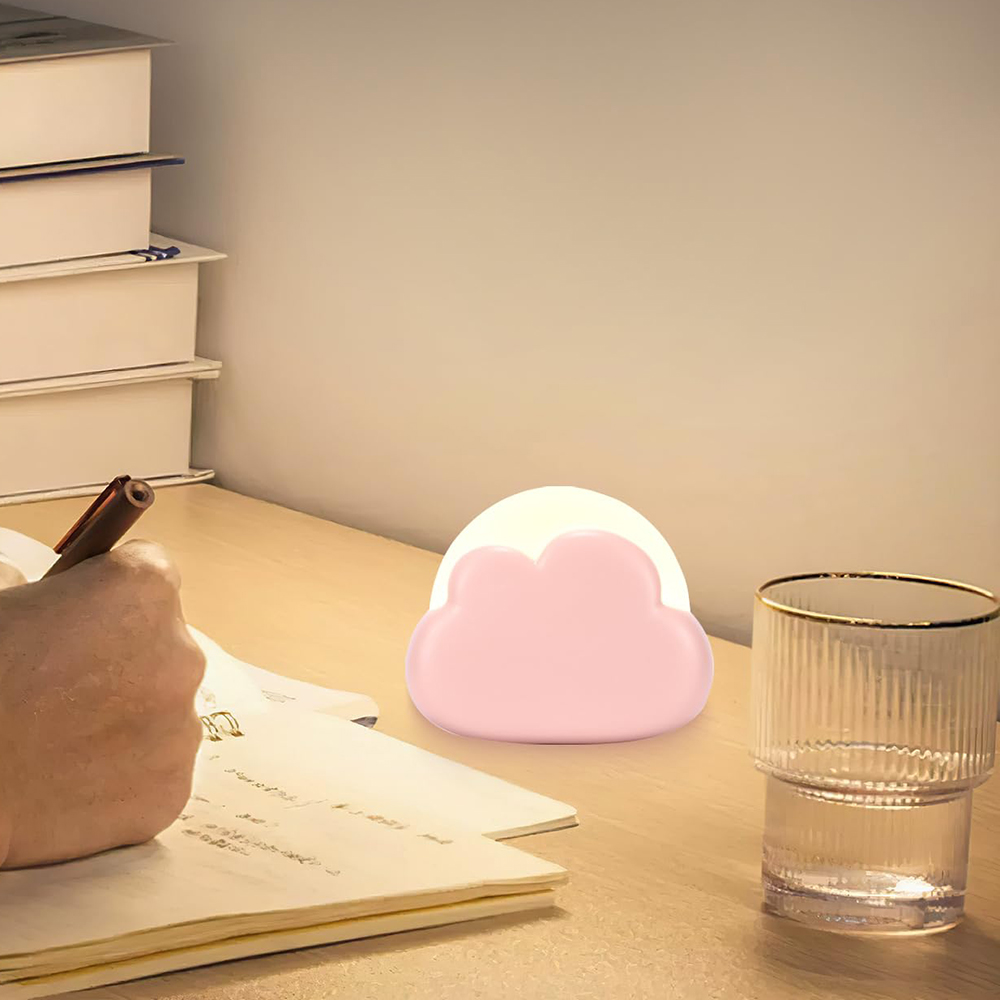 Eine Person schreibt mit einem Stift auf Papier. Auf dem Schreibtisch stehen eine rosa Wolkenlampe und ein Glas Wasser.