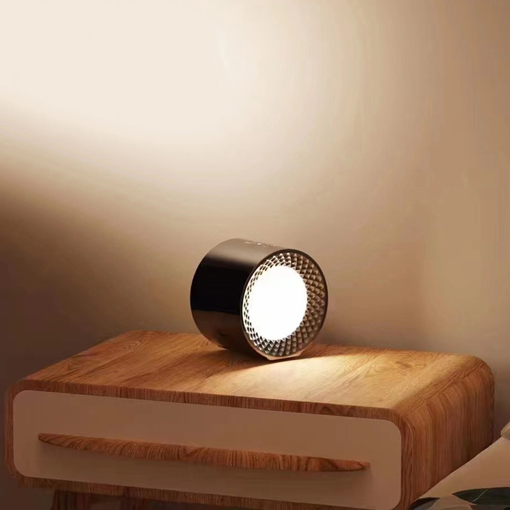 Eine schwarze und silberne zylindrische Lampe steht auf einem hölzernen Nachttisch. Die Lampe strahlt helles weißes Licht aus.