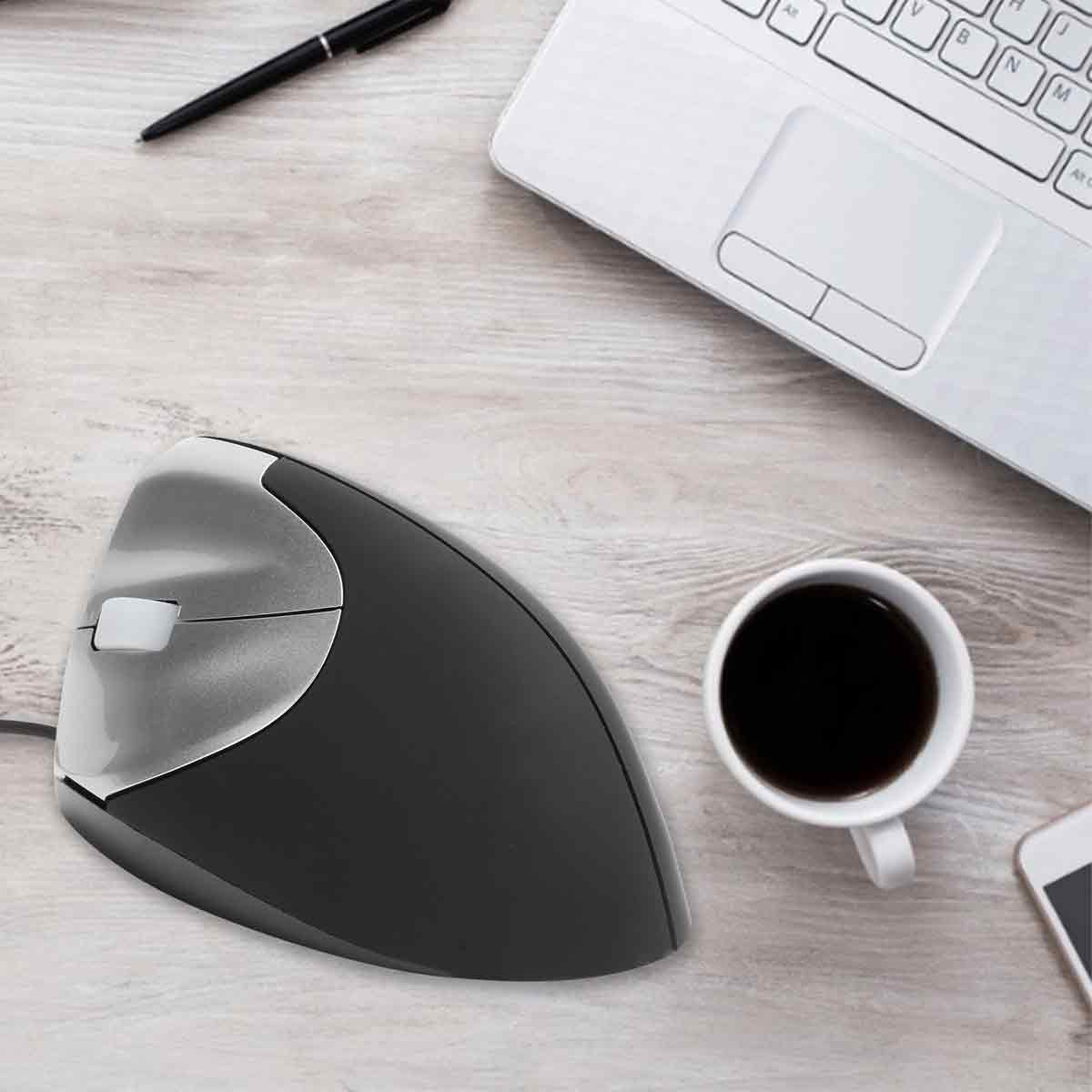 Eine ergonomische Maus, ein Laptop, eine Kaffeetasse, ein Stift und ein Smartphone auf einem Holztisch.