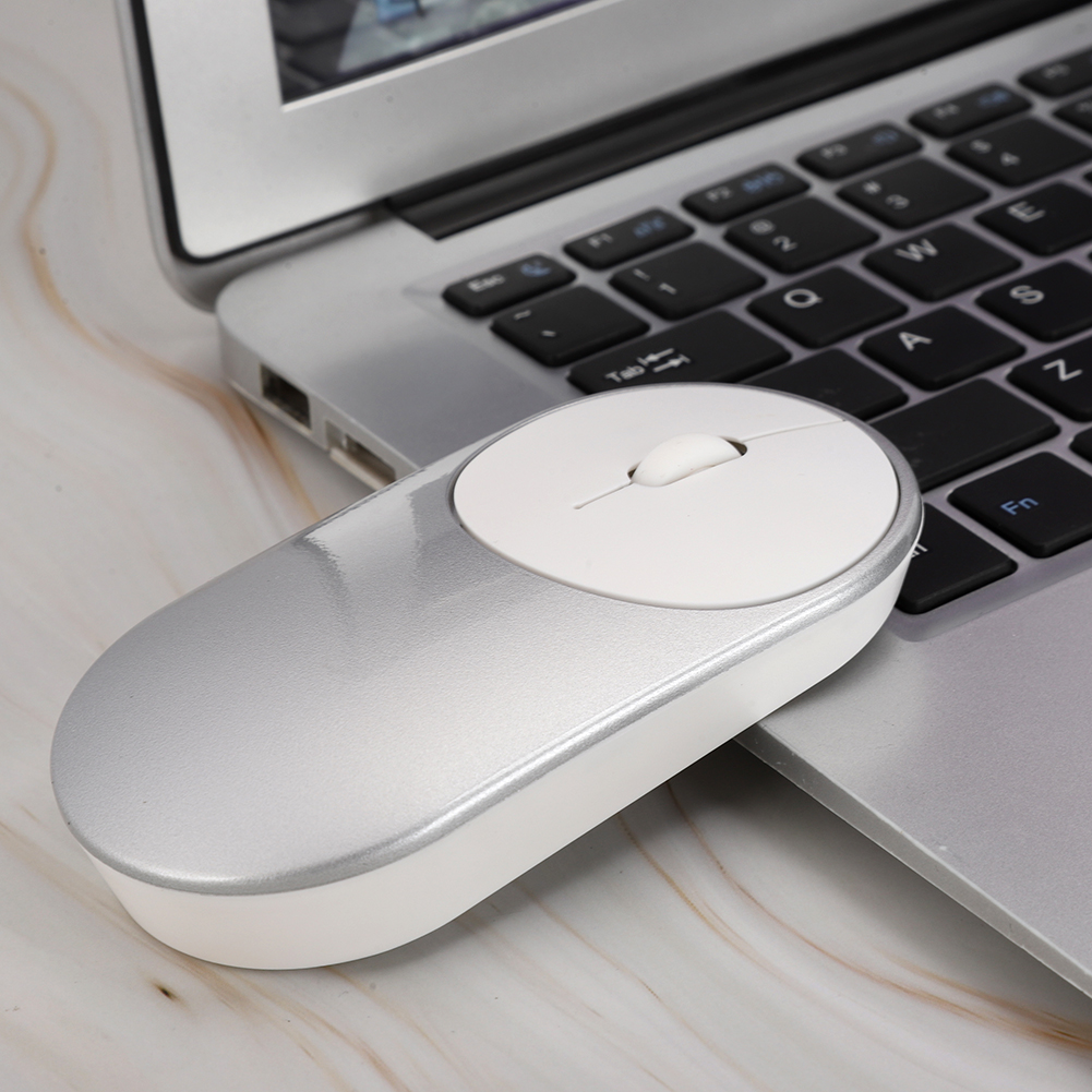 Eine silberne und weiße Computermaus liegt auf einer Laptop-Tastatur auf einer Marmoroberfläche. Die Maus ist oval mit einem Scrollrad.