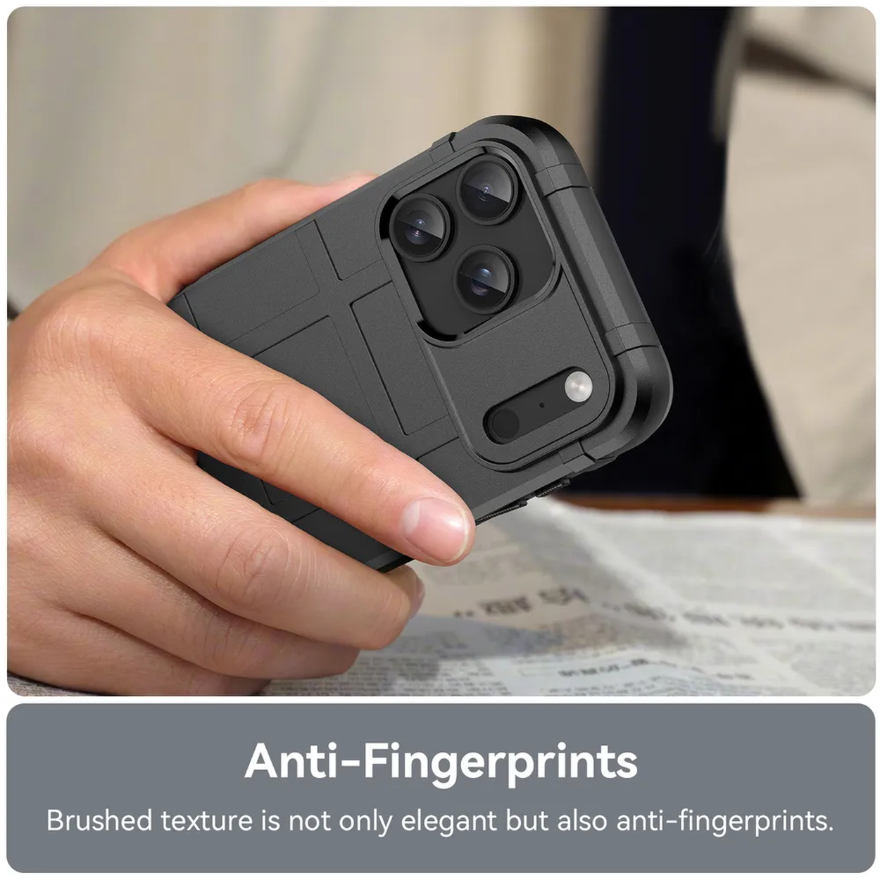 Een hand houdt een zwarte telefoonhoes met drie cameralenzen vast, boven een krant.