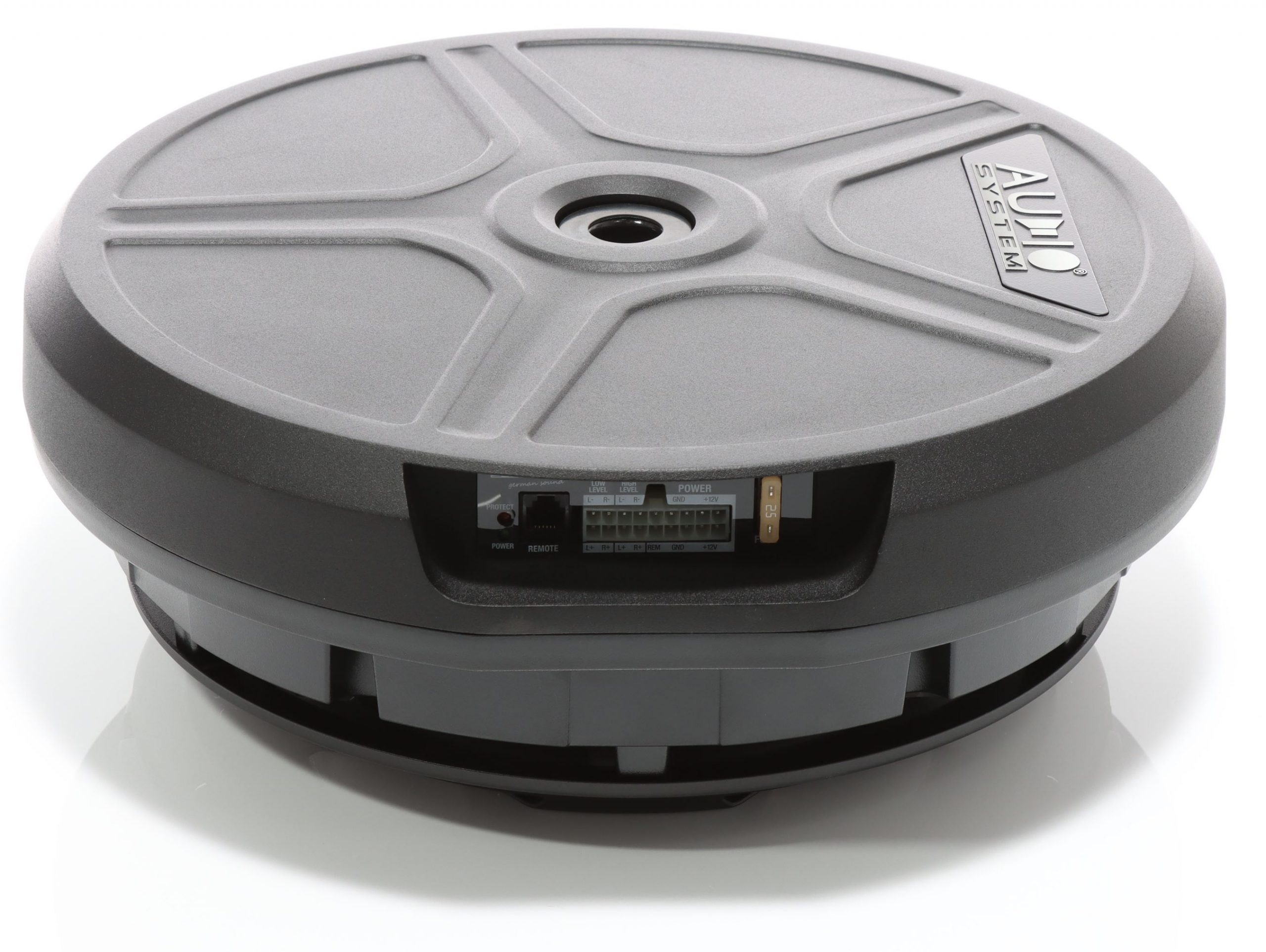 Grauer Audio System-Subwoofer auf weißer Oberfläche. Er hat ein zentrales Loch und verschiedene Anschlussports.