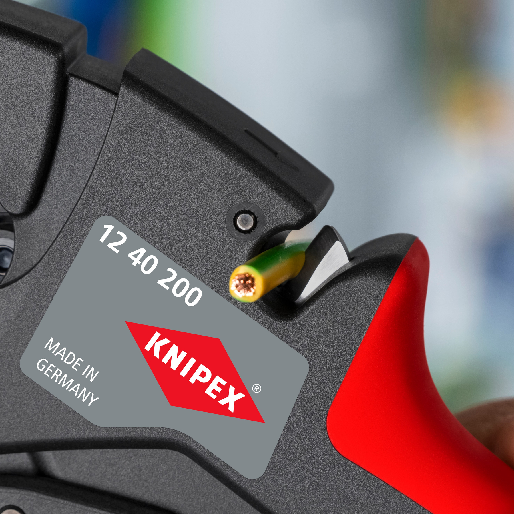 Nahaufnahme eines Kabelabisolierers. Das Werkzeug ist schwarz mit rotem Griff. Ein Draht wird abisoliert. Die Marke ist KNIPEX.