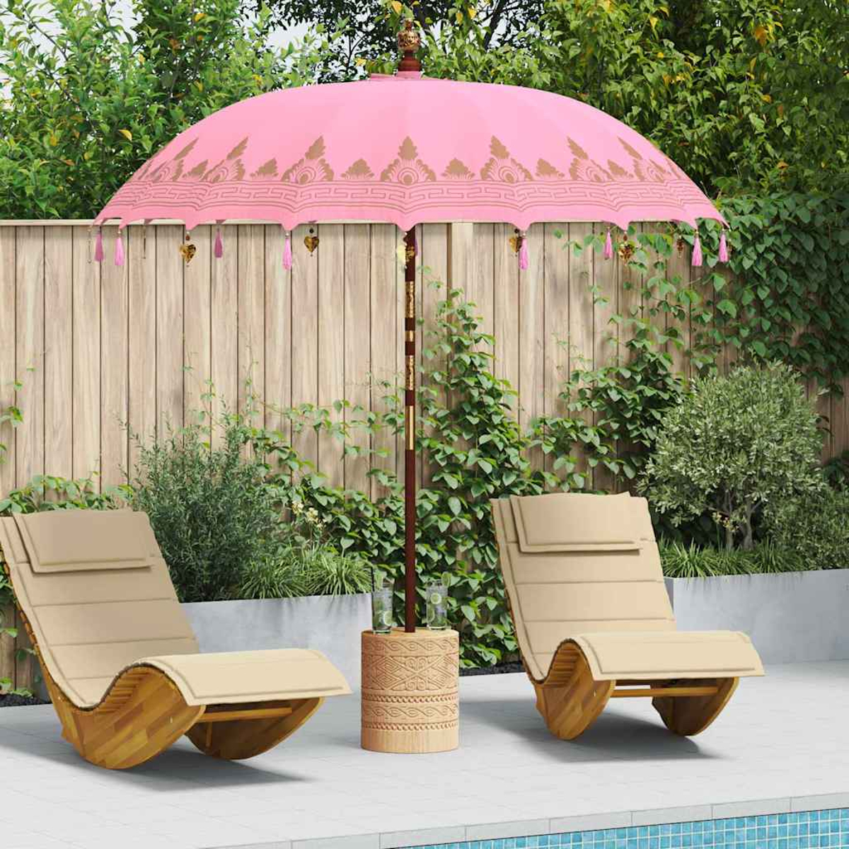 Ein rosa Sonnenschirm beschattet zwei beige Liegestühle. Ein Holztisch hält Gläser. Grünes Laub und ein Holzzaun vervollständigen die Szene.