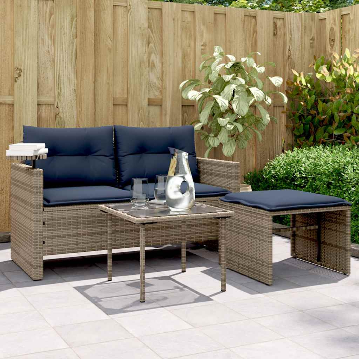 Gartenmöbel-Set aus Korbgeflecht: Sofa, Tisch und Hocker mit blauen Kissen. Kanne und Gläser stehen auf dem Tisch. Holzzaun.